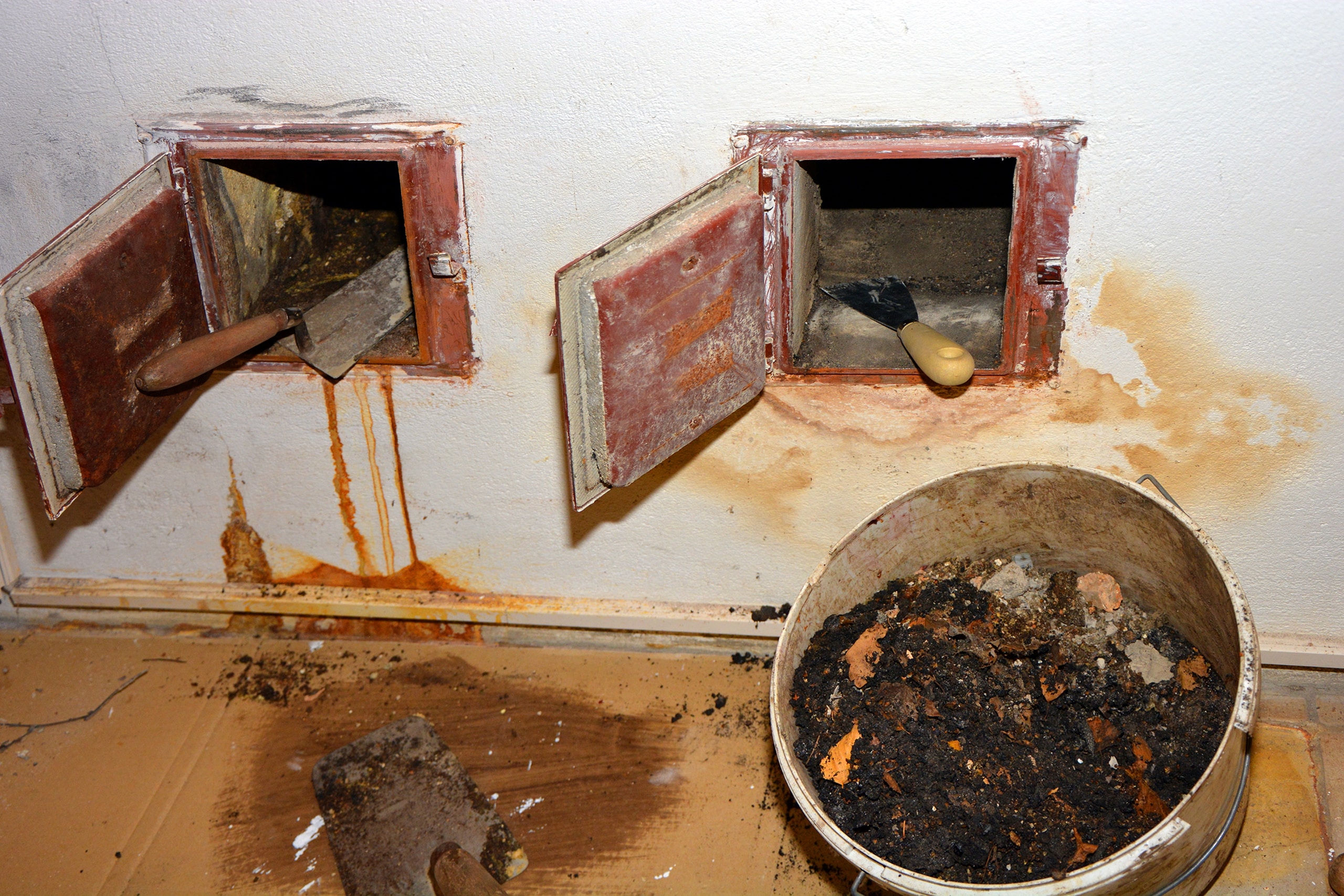 Kamin an der Innenwand eines älteren Gebäudes mit 2 Kamintüren aus Eisen und starken Versottungsrückständen druch falsches Heizen mit feuchtem Brennholz.