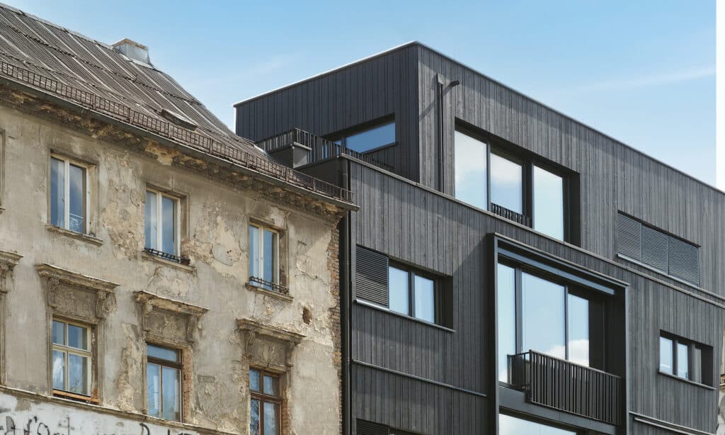 Kontraste von alter und neue Architektur mit neuer, moderner Holzfassade und stark baufälligem Haus daneben.