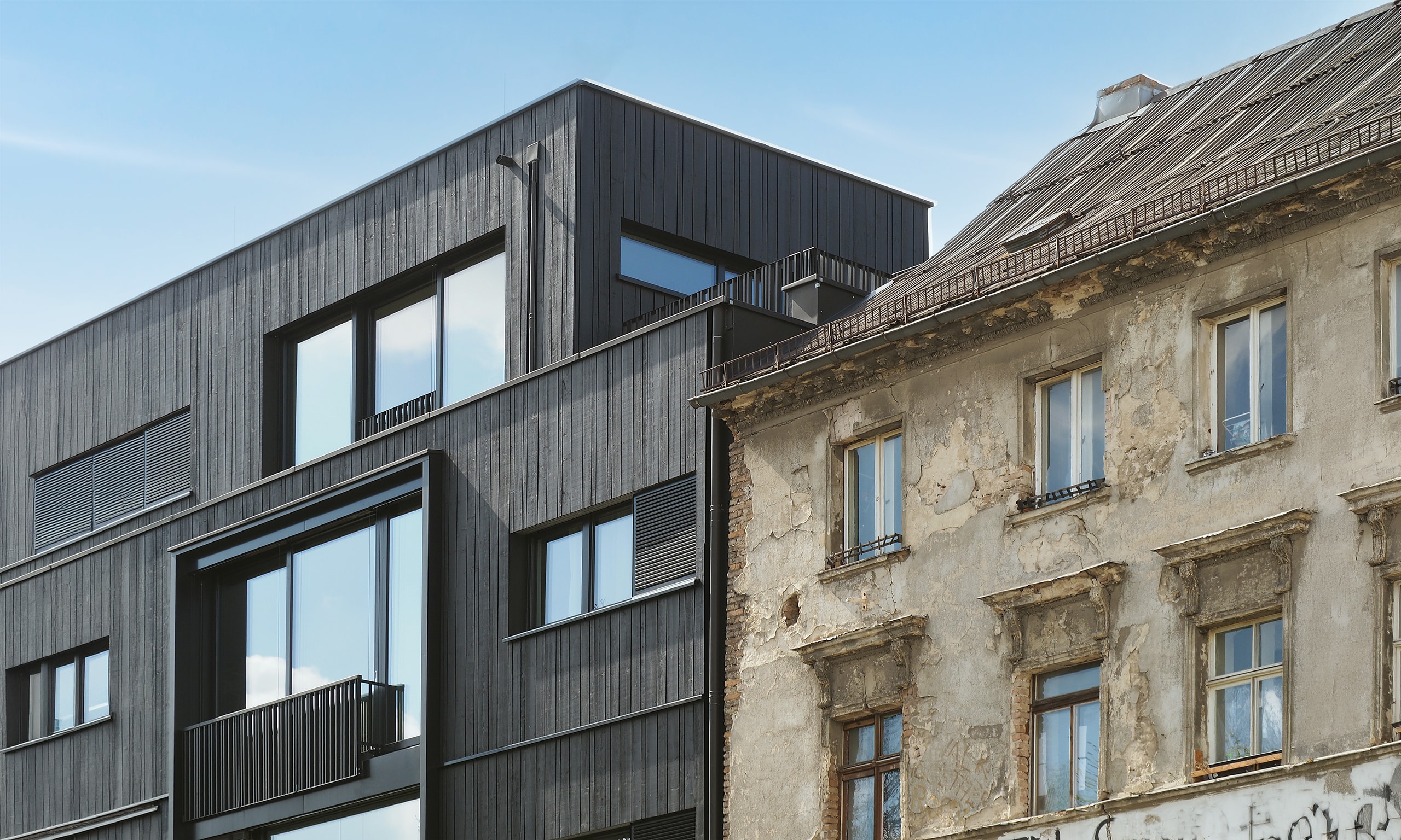Kontraste von alter und neue Architektur mit neuer, moderner Holzfassade und stark baufälligem Haus daneben.