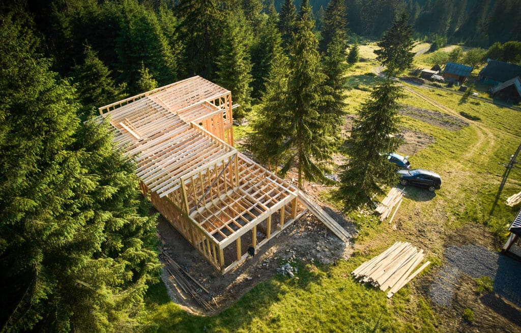 Drohnenperspektive eines zweistöckigen Holzrahmenhauses, das in der Nähe eines Waldgebiets errichtet wird. Konzept des modernen ökologischen Bauens und zeitgenössischen architektonischen Designs.