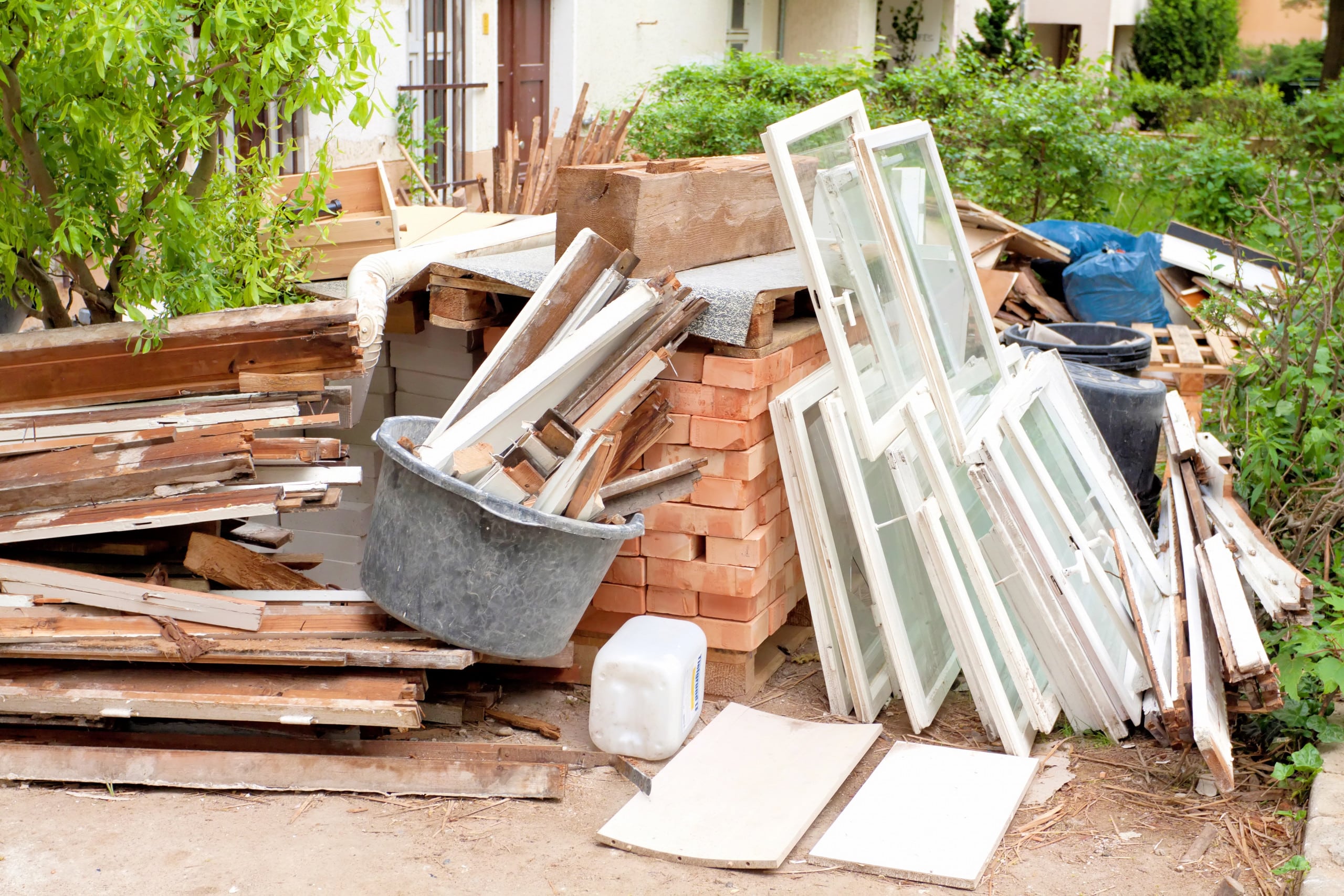 Baubabfälle aus alten Holz, Fensterrahmen mit Glas und Ziegeln, die auf den Abtransport durch ein Entsorgungsunternehmen warten.