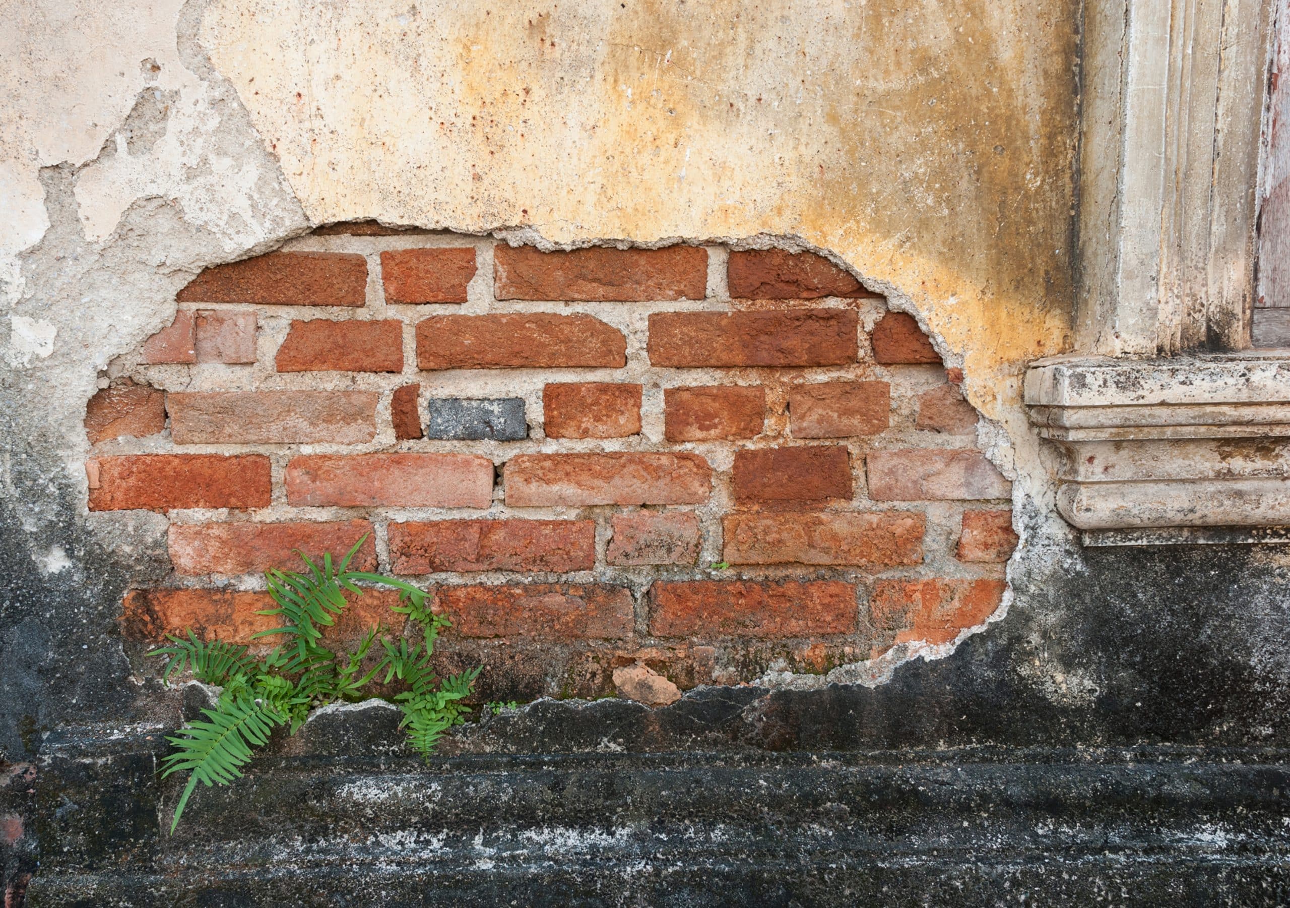 Beschädigtes Mauerwerk der alten Außenmauer eines Gebäudes mit Sicht bis zum Ziegel.