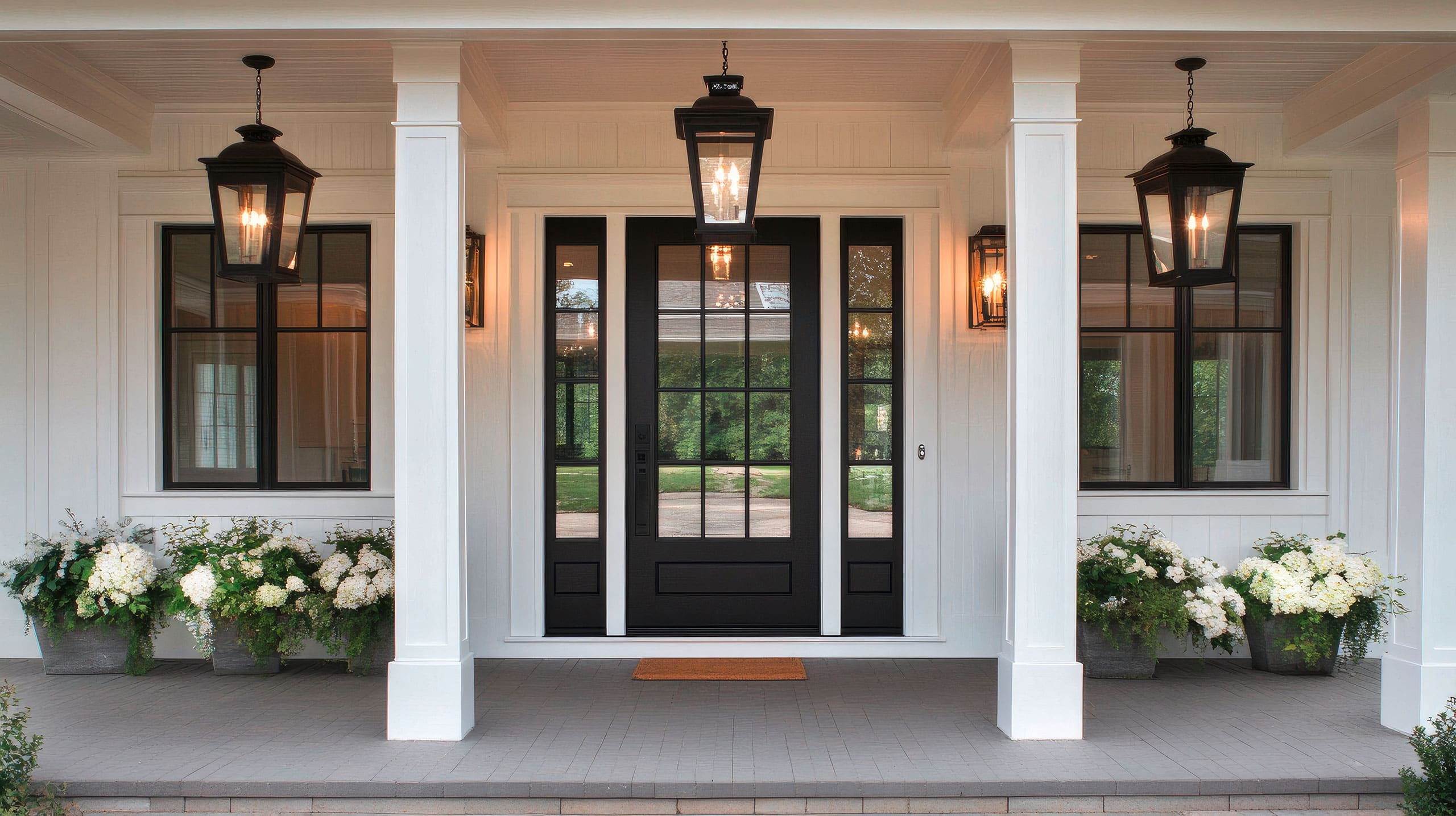 Stilvoller, moderner Eingang zu einem edlen Landhaus mit dunkler Aluminium-Haustür mit elegantem schwarzem Glas, weiße Wände und aufwendig gearbeitete Holzelemente.