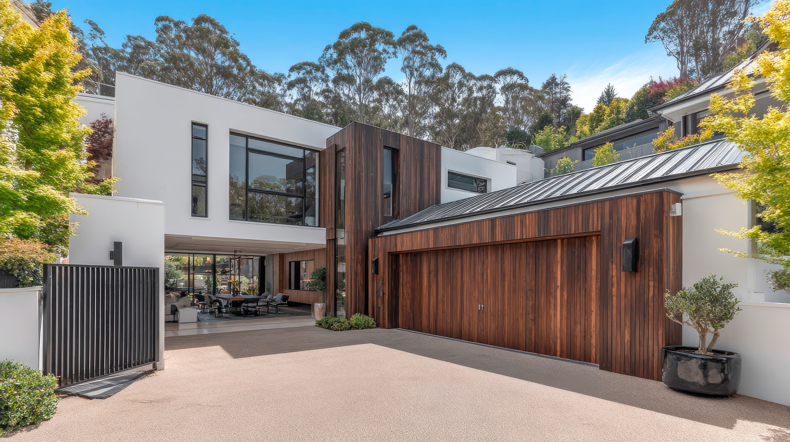 Großzügiges, modernes Wohngebäude mit extravaganter Hausfassade in weiß und und dunklen Holzelementen und einer breiten Garage mit einem zweiflügeligen Garagentor.