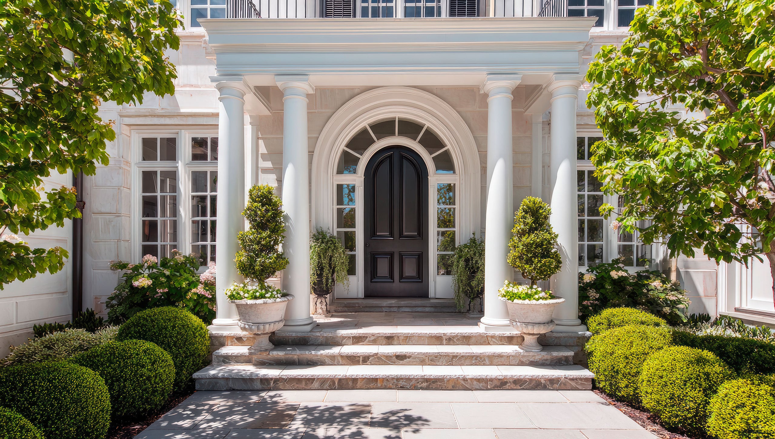 Prächtiger Eingang zu einem luxuriösen Haus im viktorianischem Stil mit weißen Säulen, Eingangstür mit verglastem Bogen und dunkler Massivholztür, sowie gepflegter Gartenanlage.