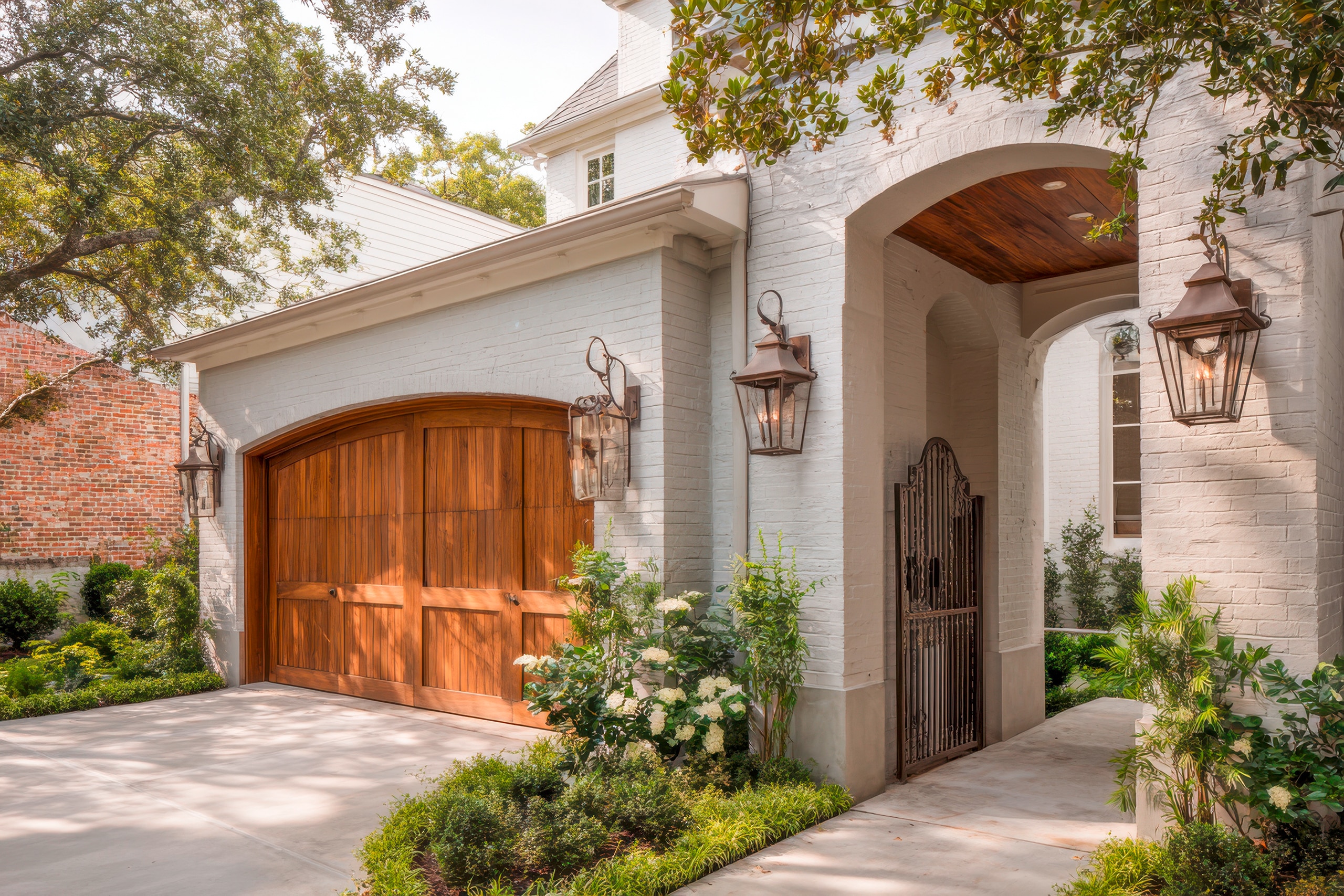 Elegante Hauseinfahrt eines luxuriösen Landhauses mit hölzernem Garagentor und üppiger Landschaftsgestaltung bei Tageslicht.