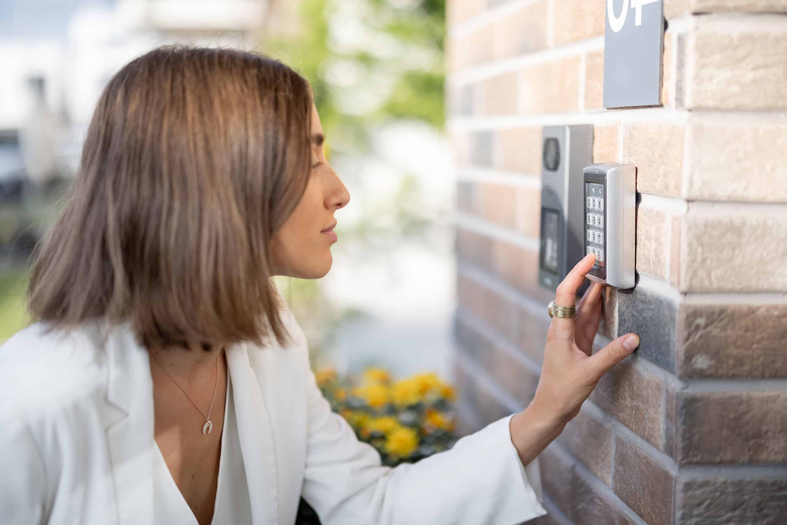 Junge Frau gibt Code auf einer Tastatur an der Hausfassade ein, um eine Tür zu öffnen.