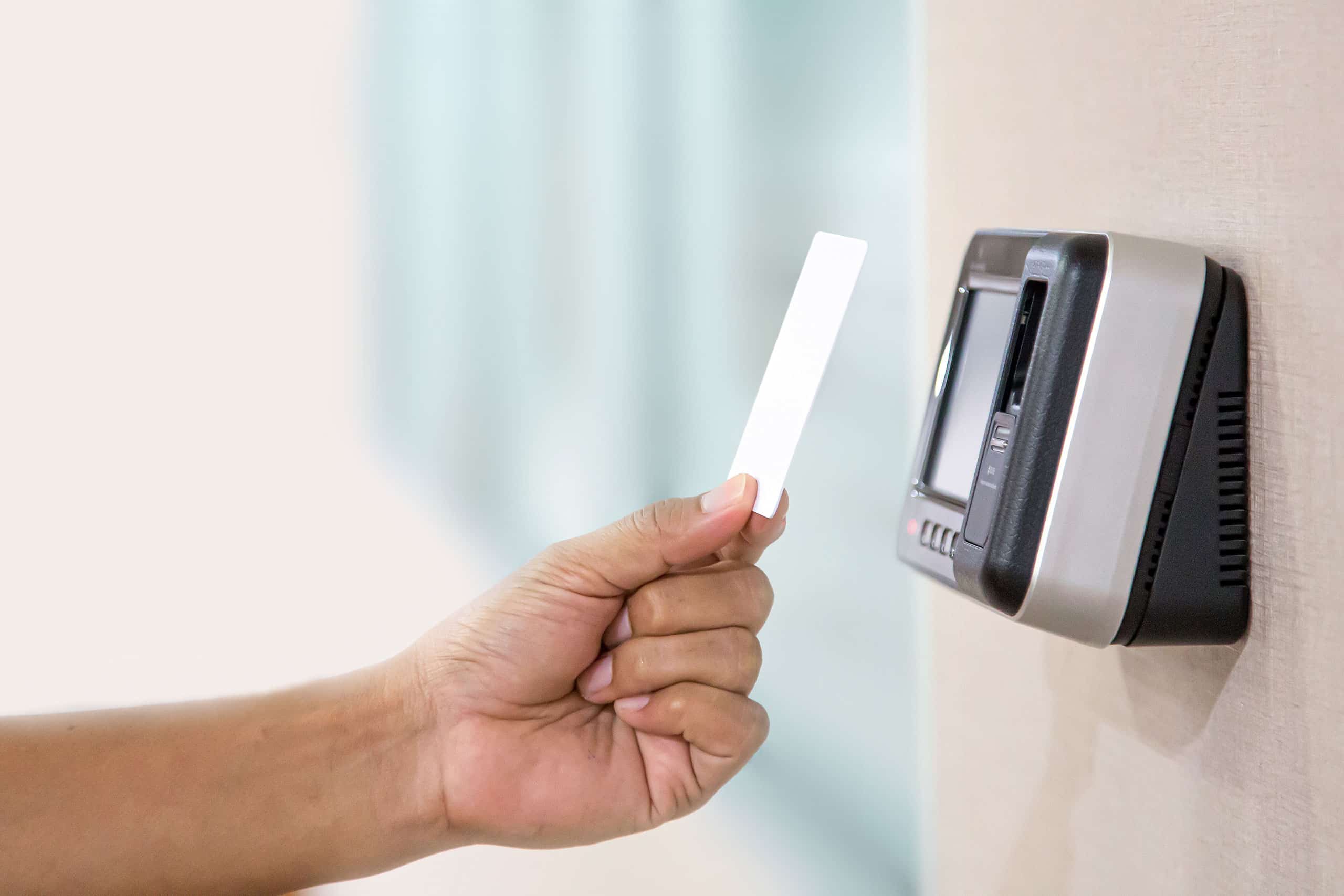 Detailfoto einer Hand, die eine ID-Chipkarte hält und mit dieser die Türöffnung per Proximity-Kartenleser nutzt. Dieses Zugangskontrollsystems zur Identitätsprüfung verfügt zusätzlich über einen Fingerabdruckscanner.