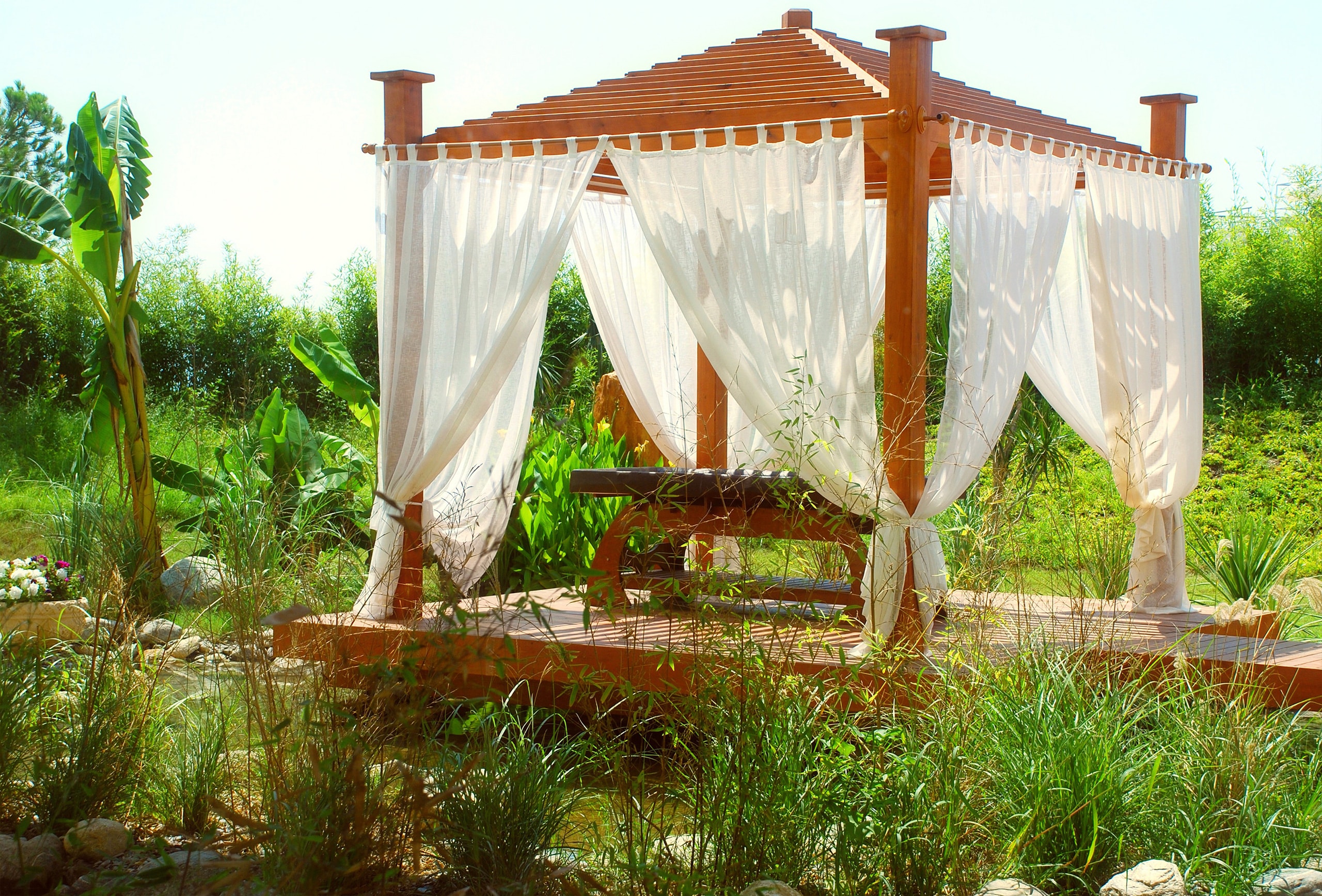 Romantischer Spa-Pavillon in einem exotischen Garten, der mit weißen Outdoor-Vorhängen bzw. Baldachinen in Szene gesetzt wurde.