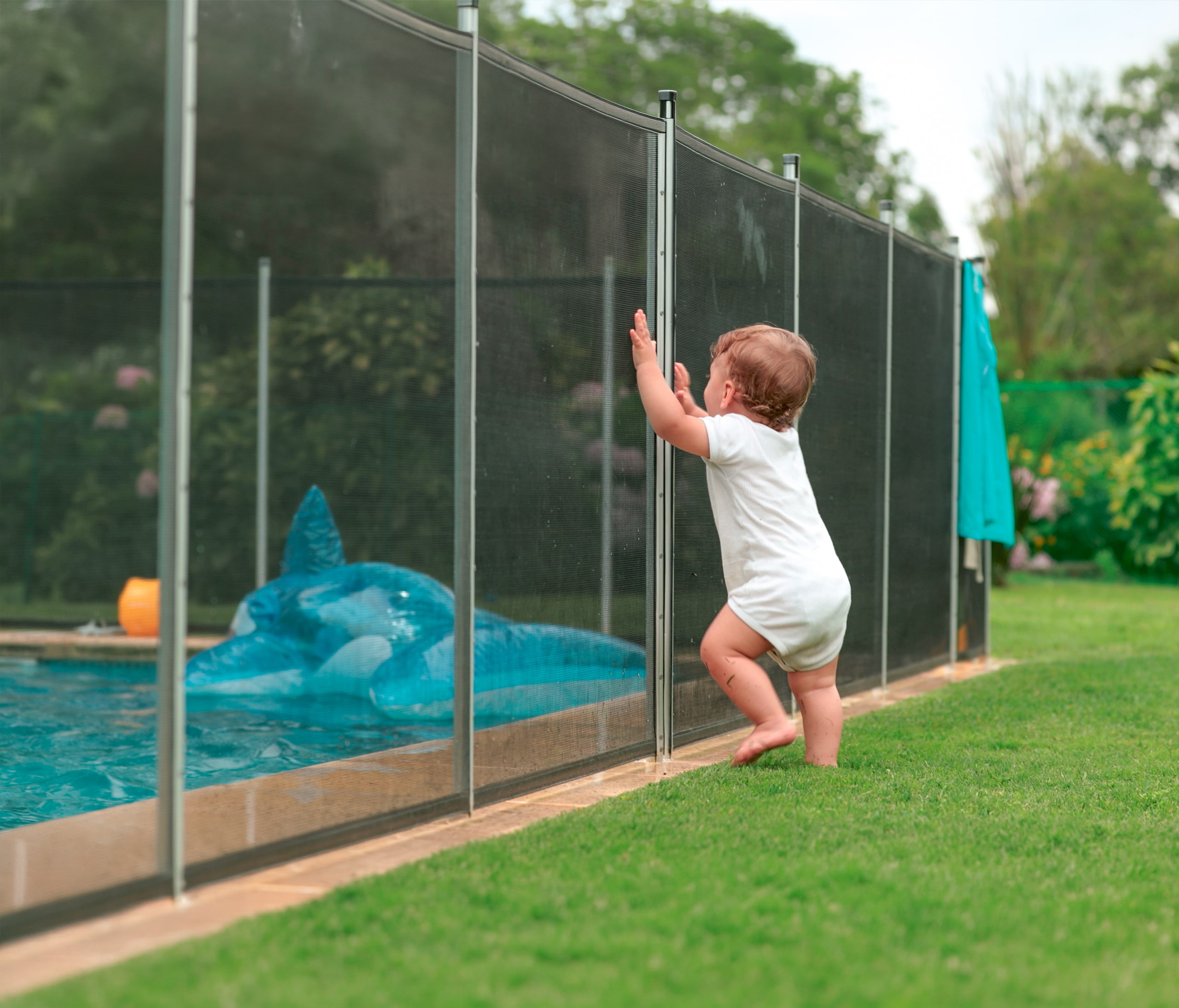Baby lehnt sich an den Sicherheitszaun des Pools im Garten.