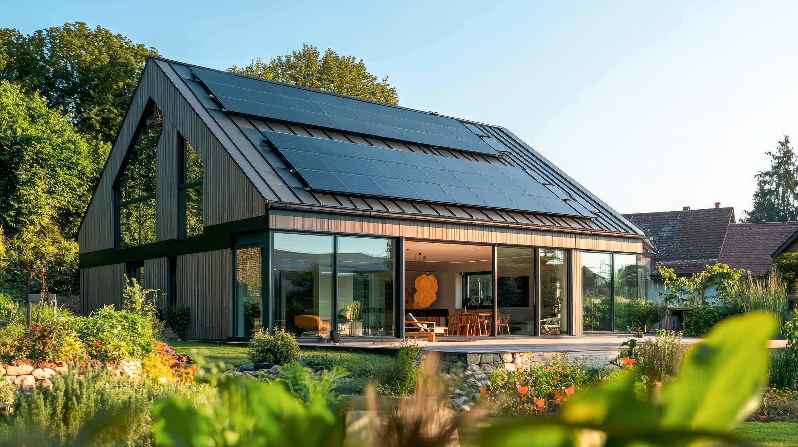 Ein modernes Haus mit Holzfassade und Solarmodulen auf dem Dach liegt inmitten üppiger Vegetation. Die großen Fenster bieten einen Blick ins Innere.