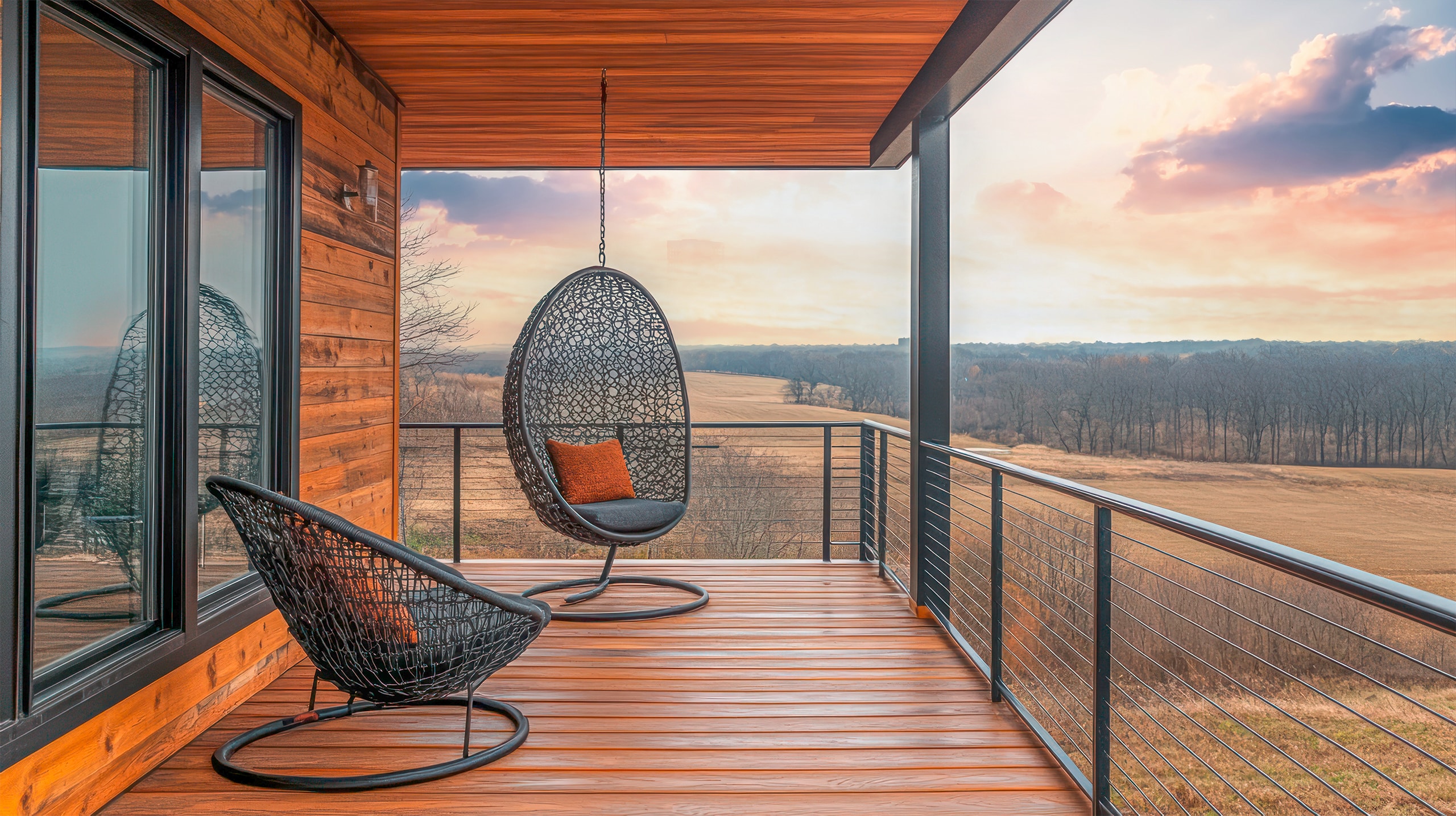 Großzügiger Balkon eines modernen Holzhauses mit zwei gemütlichen Sitzgelegenheiten mit Blick in die herbstliche Natur bei Abendstimmung.
