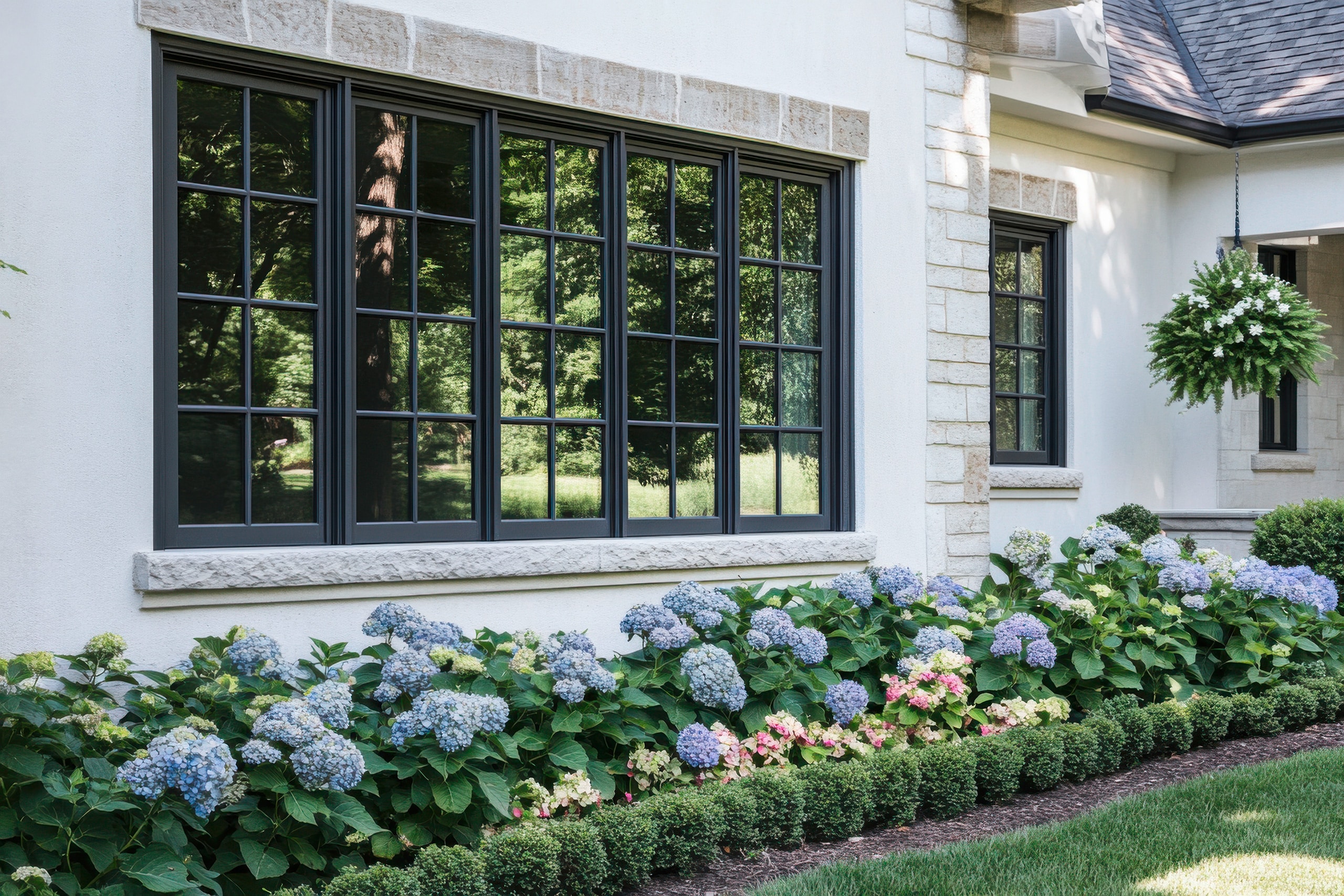 Wunderschöne Gartengestaltung mit Hortensien neben elegantem Fensterdesign einer edlen Landhausvilla in ruhiger Wohnlage bei Tag.