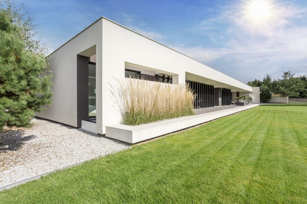 Moderne, eingeschossige Villa in weiß mit Flachdach, vertikalen Designelementen aus dunklem Holz und großzügiger Terrasse mit Blick auf den frisch gemähten Rasen.