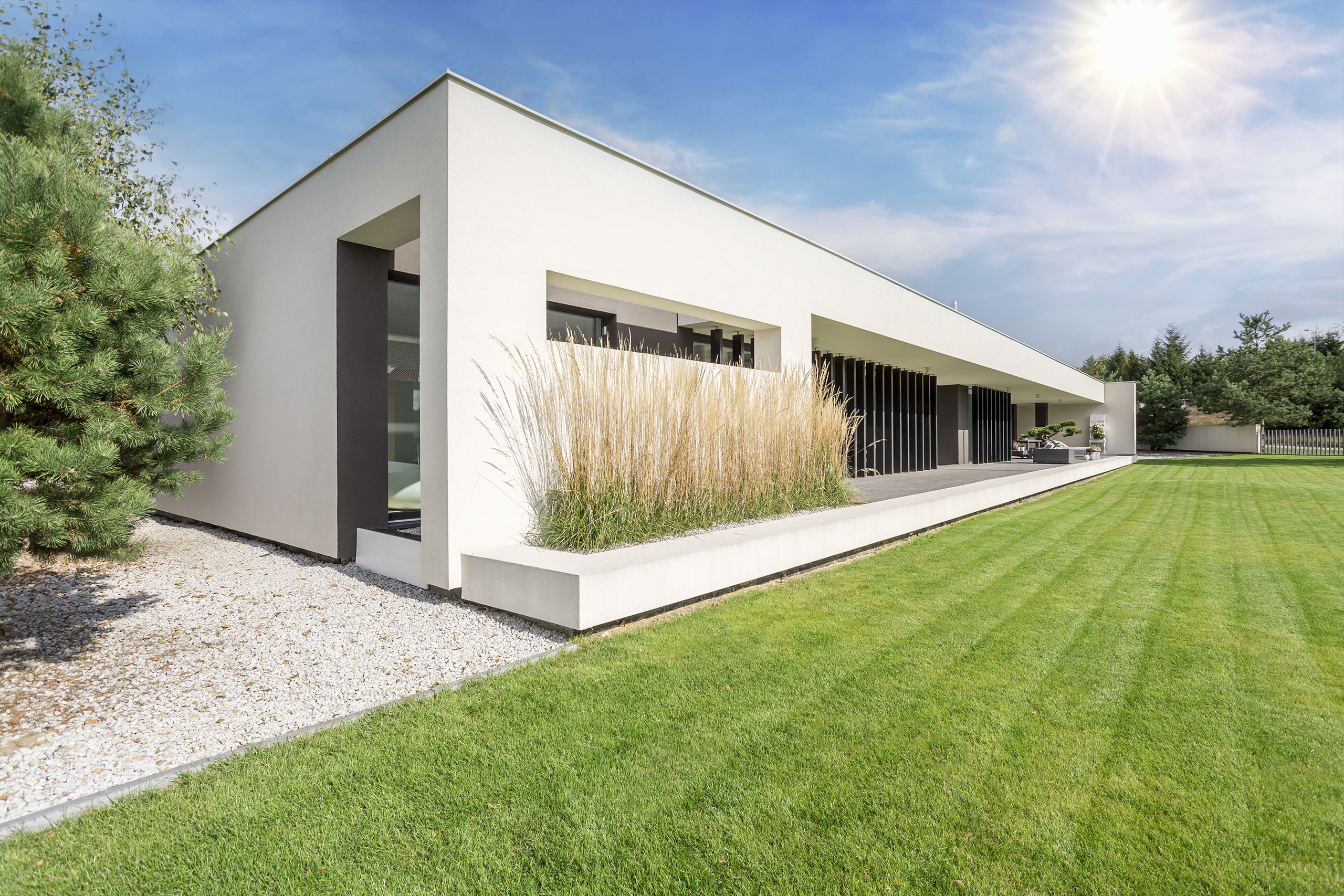 Moderne, eingeschossige Villa in weiß mit Flachdach, vertikalen Designelementen aus dunklem Holz und großzügiger Terrasse mit Blick auf den frisch gemähten Rasen.