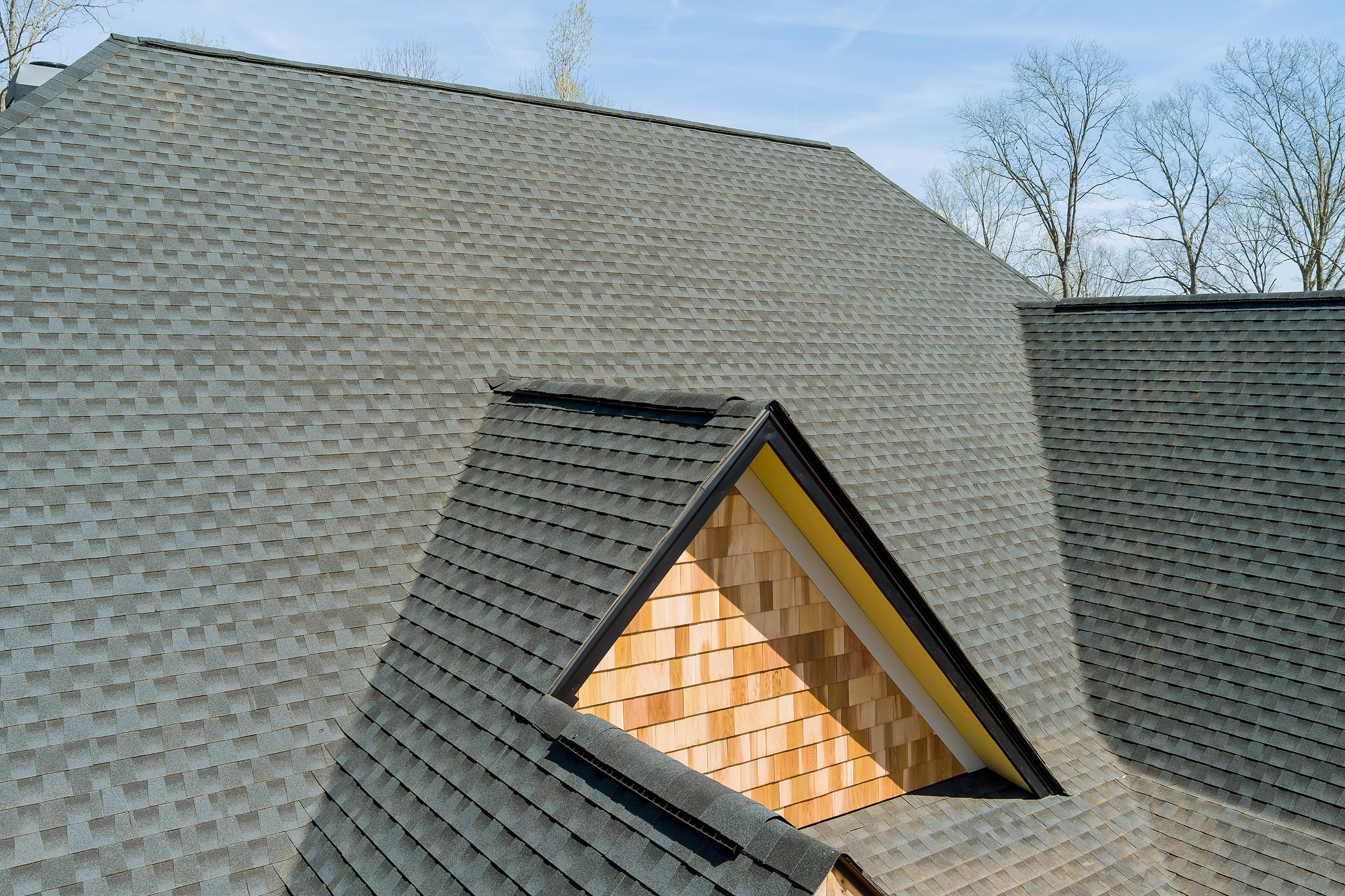 Detailfoto des Daches eines großen Wohnhauses im klassischen Stil mit einer Dacheindeckung aus Asphaltschindeln in Anthrazit.