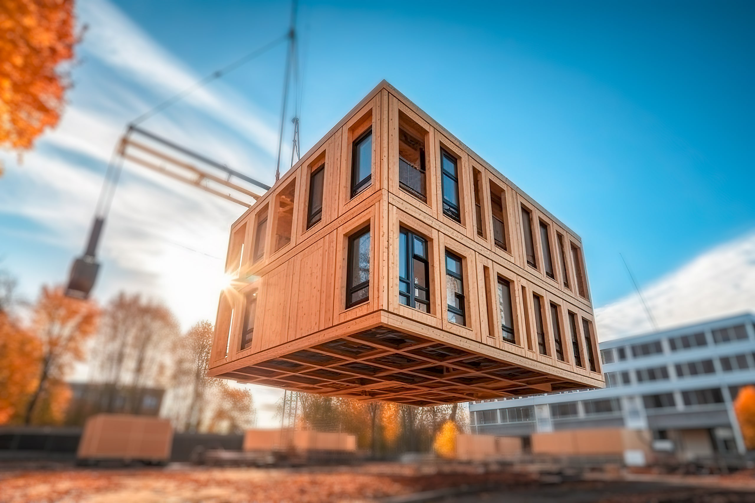 Holzmodule für ein Wohngebäude in modularer Fertigbauweise werden auf einer Baustelle mit dem Kran angeliefert, um am Zielgrundstück installiert zu werden.