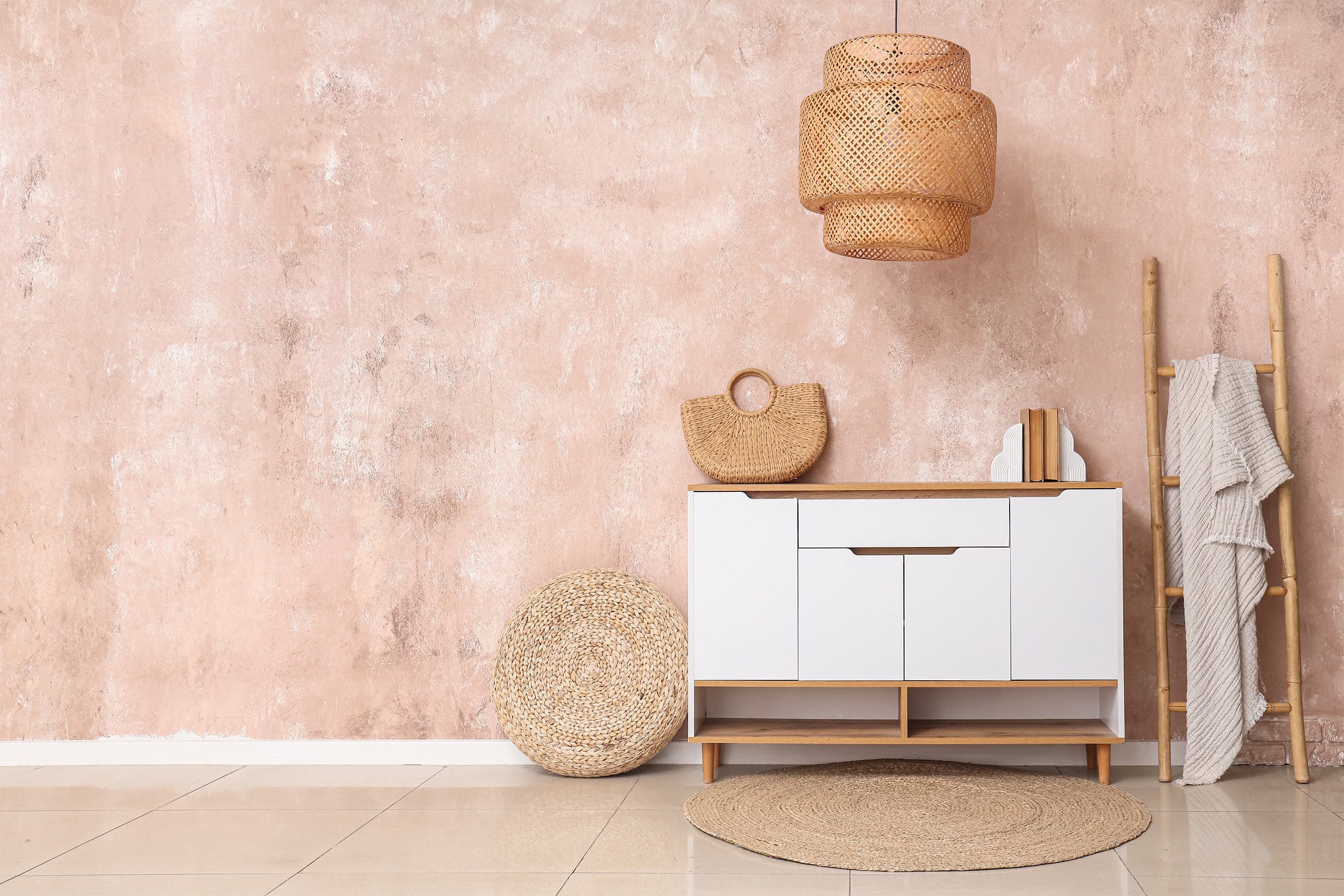 Interieur eines stilvollen Zimmers mit weißer Kommode, Leiter und Lampe. Die Materialien Holz, Seegras und Bast und sind dabei besonders oft verwendet. Die Wände sind in rosa Spachteltechnik in Szene gesetzt.