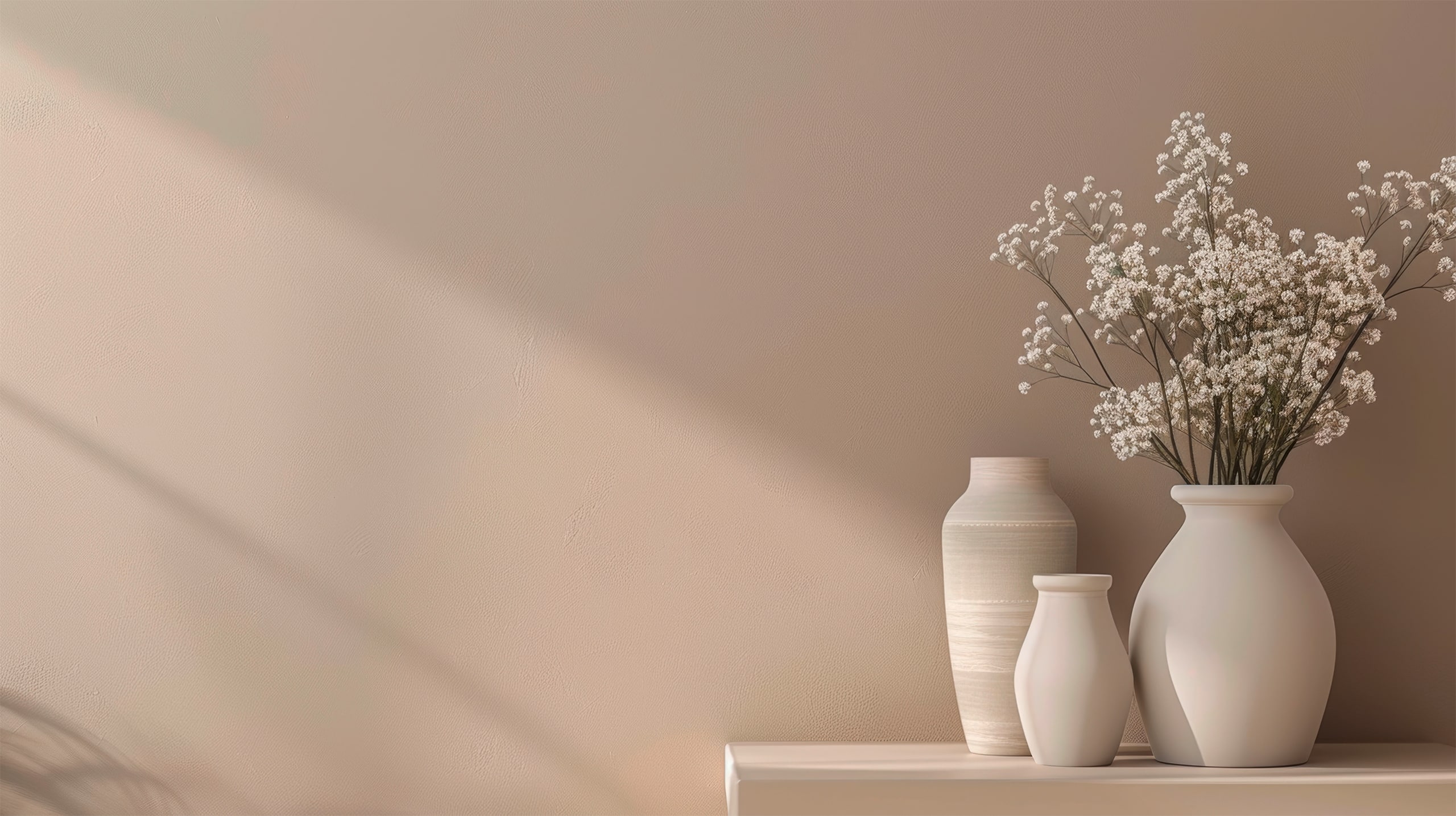 Detailfoto einer Wand in Lachs / Aprikot mit Lichteinfall durch ein Fenster. Auf einem Wandboard sind als Accessoires 3 Vasen in passendem Beigeton platziert. 1 Vase enthält getrocknetes Schleierkraut.