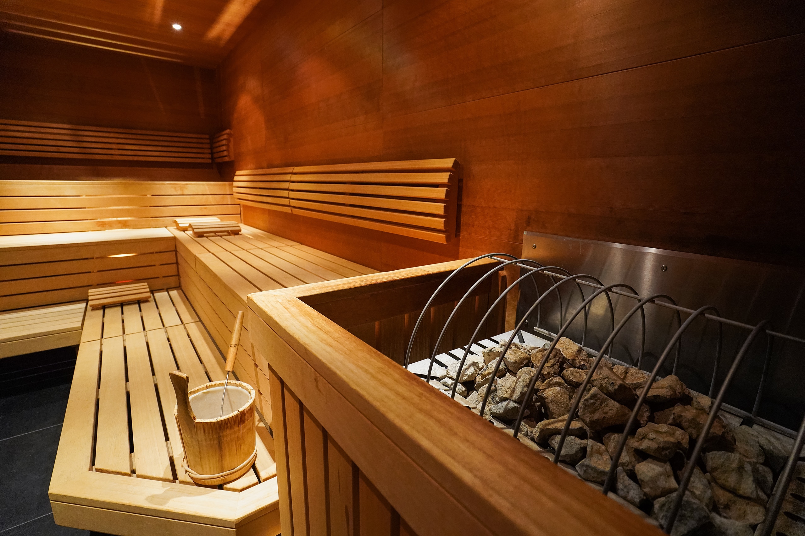 Detailansicht einer Finnischen Sauna mit Holzofen und Aufgusskübel aus Holz.