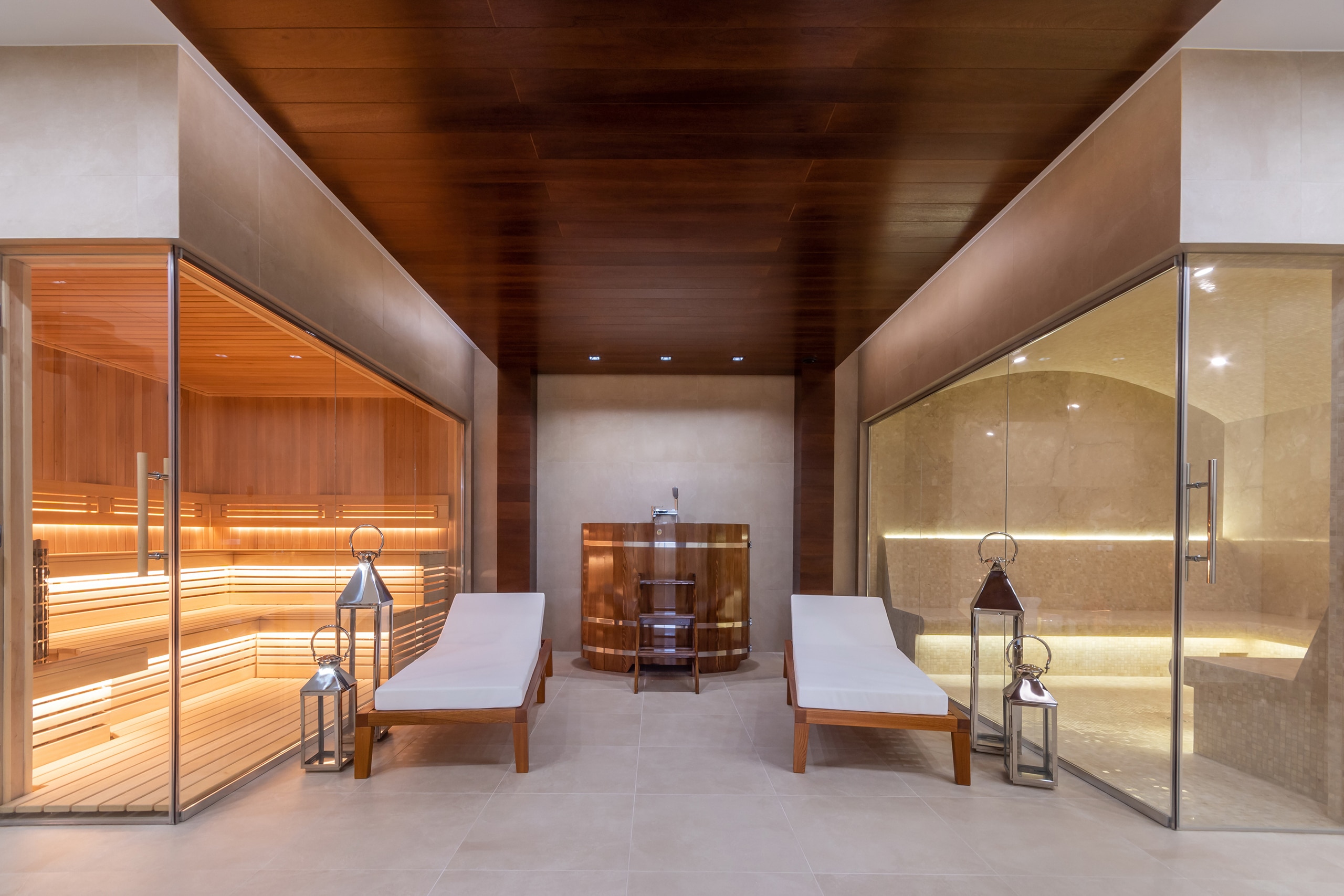 Exklusive Gestaltung des Untergeschosses einer Luxusvilla mit Sauna und Hamam hinter Glaswänden. Im Eingangsbereich der Phytosauna befinden sich ein Zedernfass und Liegestühle.
