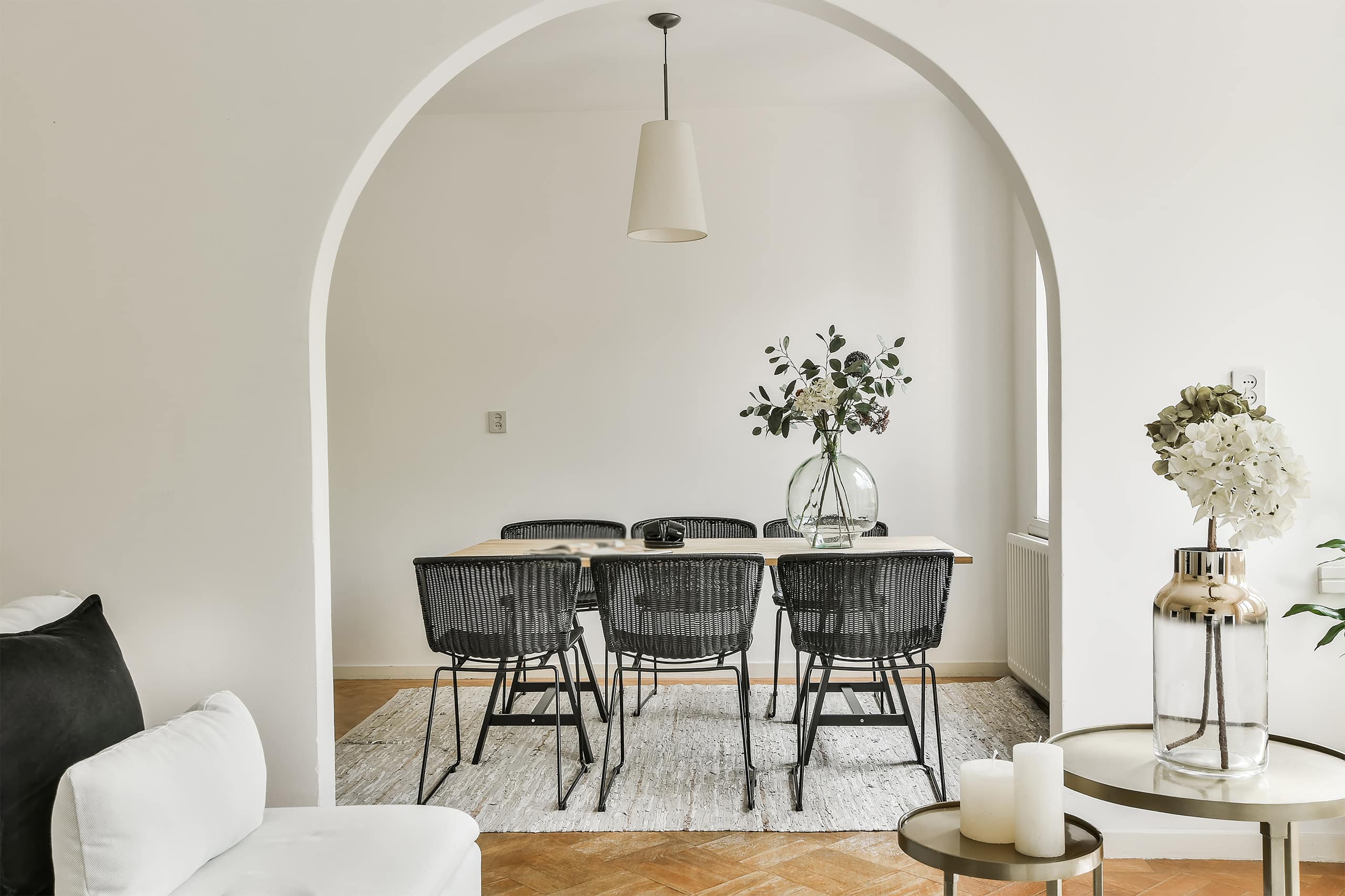 Blick durch einen Rundbogen in den gemütlichen Essbereich bzw. Esszimmer mit einem Tisch und 6 Stühlen mit dunkler Rattanbespannung und freiliegendem Teppich.