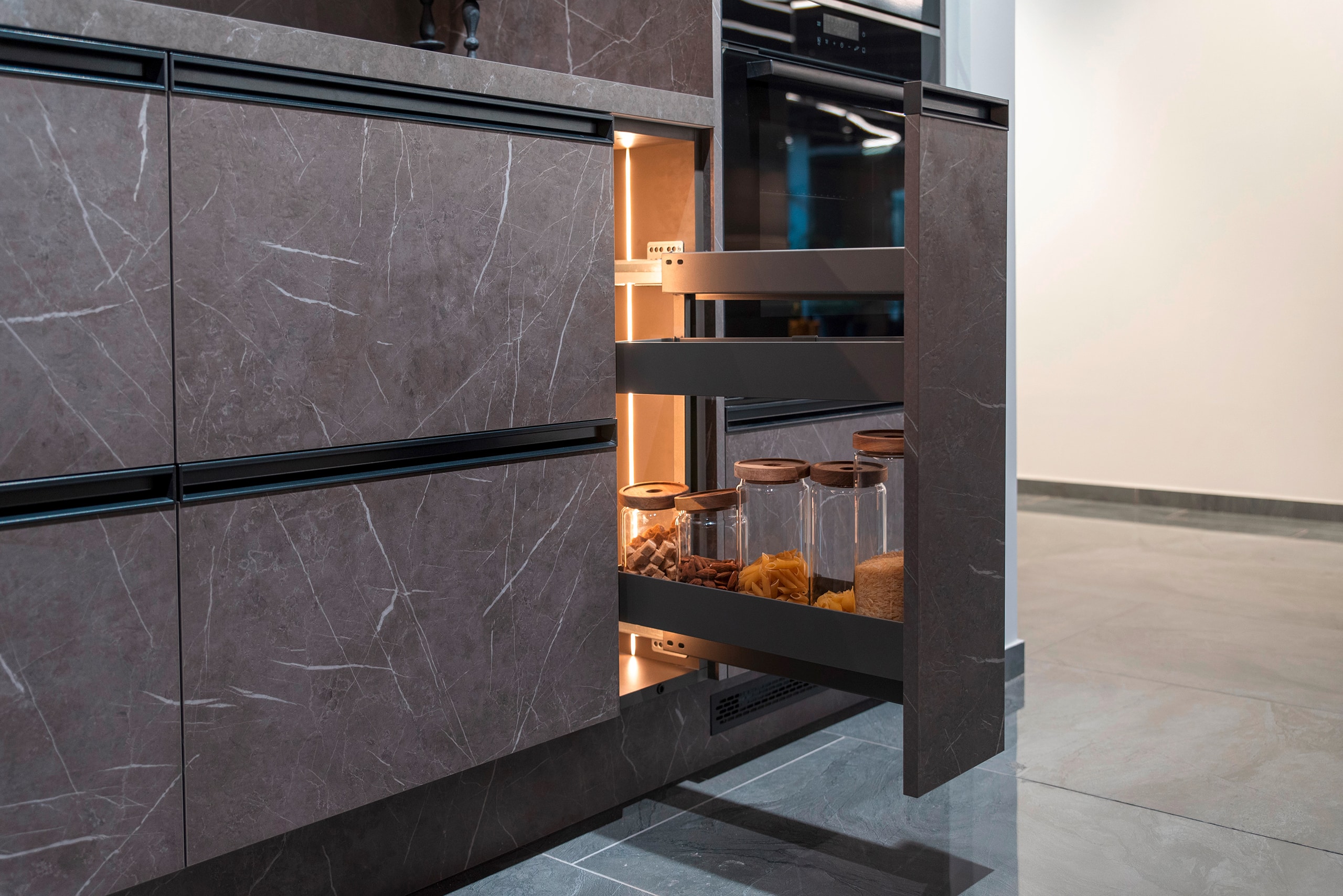 Moderne offene Küche mit Fronten in edlem Marmor-Look, mit ausziehbarem Vorratsschrank, darin Glasbehältern und praktische Beleuchtung.