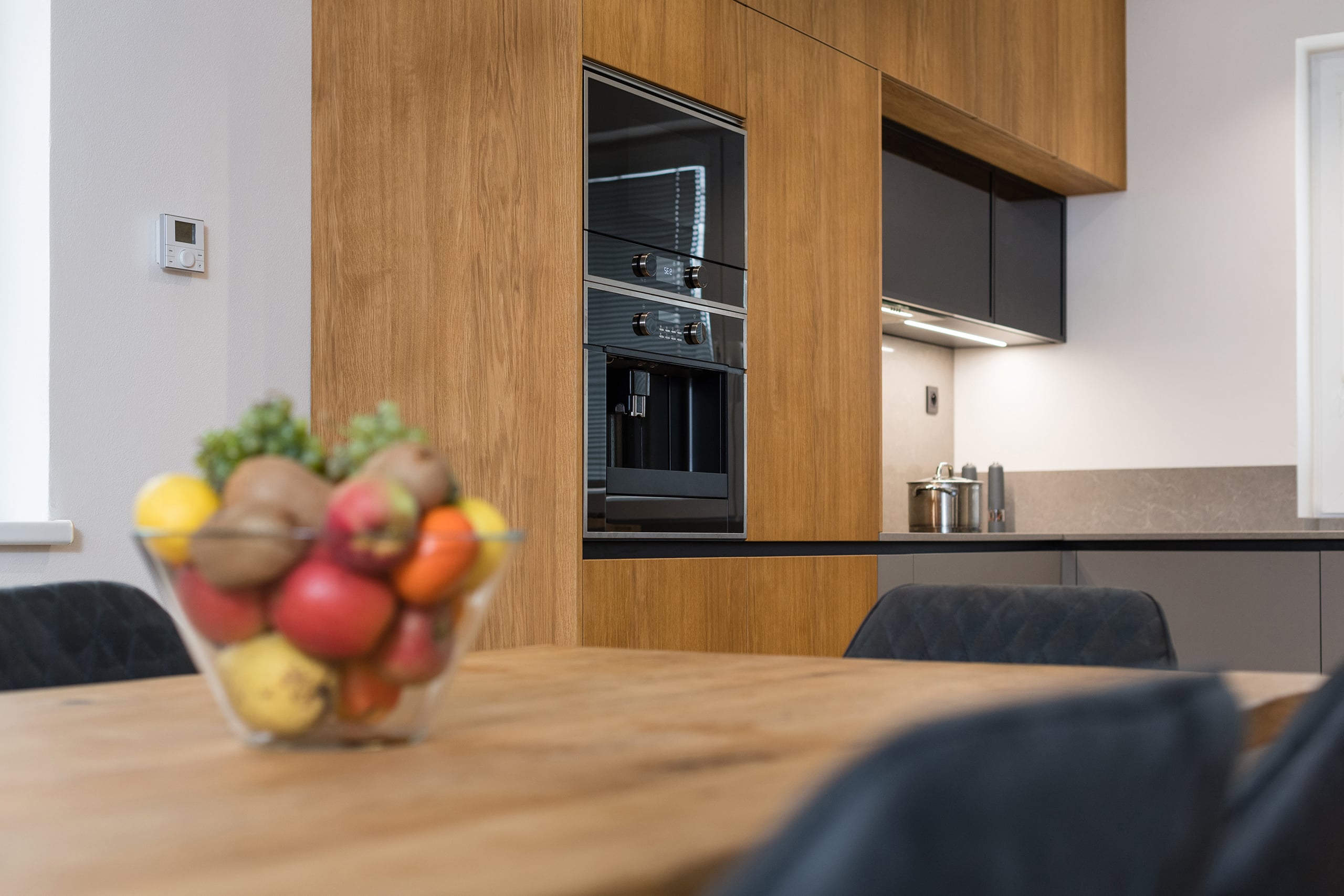 Detailansicht einer modernen Kücheneinrichtung mit Einbaugeräten, wie einer Mikrowelle und eines Kaffeevollautomaten mit Festwasseranschluss, in ergonomischer Höhe.