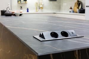 Nahaufnahme einer intelligent versenkbarer Steckdosen in einer dunklen Arbeitsplatte einer modernen Küche in Marmordesign.