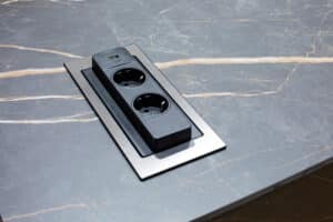 Nahaufnahme einer intelligent versenkbarer Steckdosen in einer dunklen Arbeitsplatte einer modernen Küche in Marmordesign.