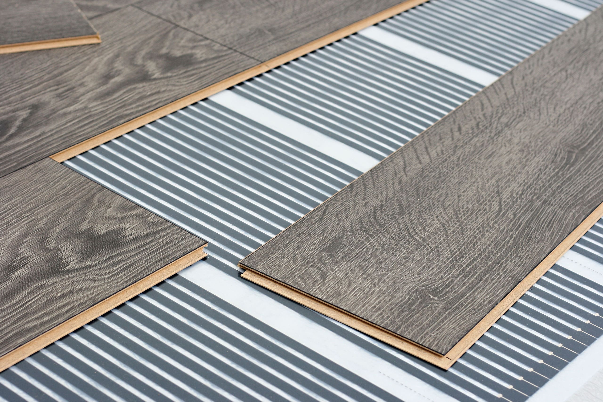 Detailansicht der Installation einer Infrarot-Fußbodenheizung unter Laminatboden.