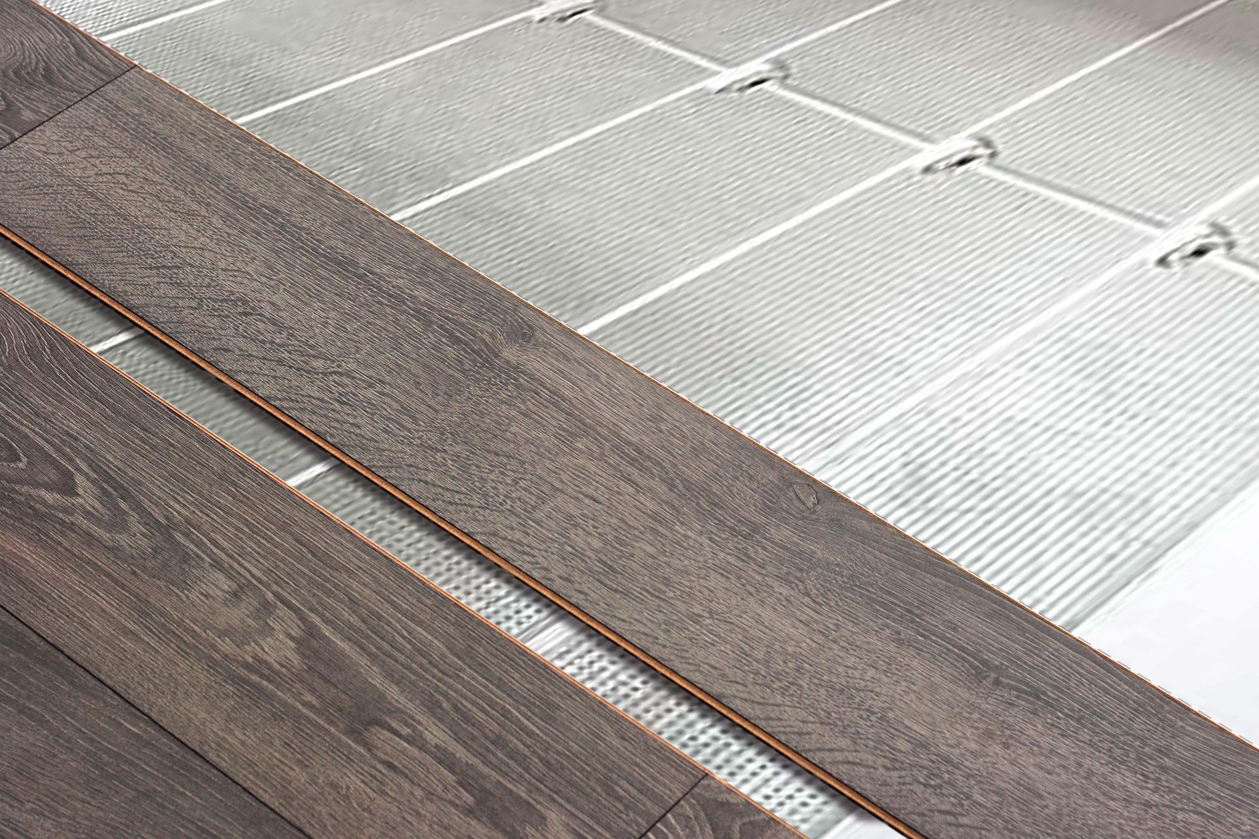 Detailansicht der Installation eines Modul-Klimabodens als Fußbodenheizung unter dunklen Laminatdielen im Holzlook.