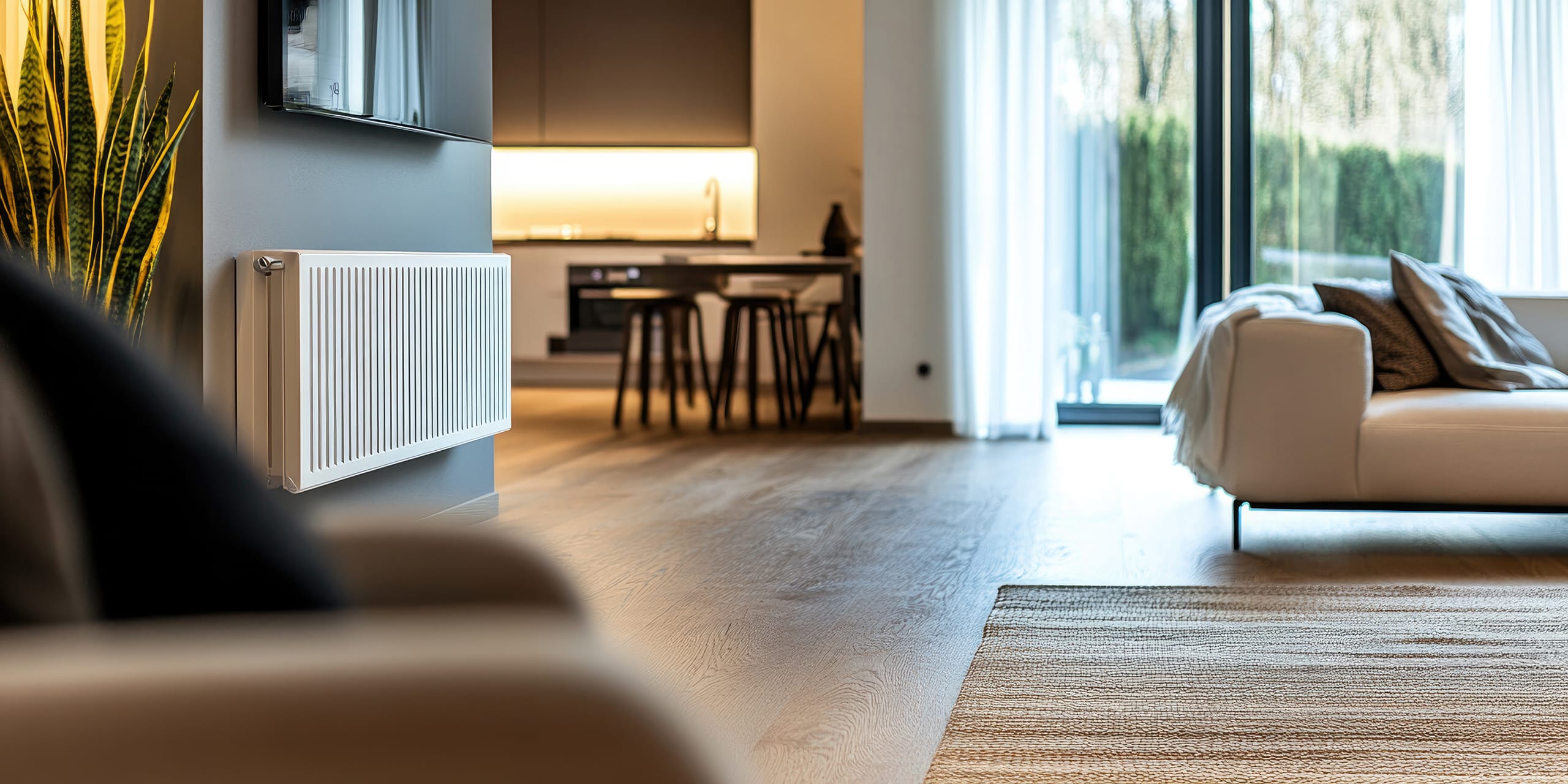 Heller Wohnraum mit einem weißen Heizkörper bzw. Radiator an der Wand, sanften beigefarbenen Möbeln und großen Fenstern, die natürliches Licht hereinlassen und eine warme und einladende Atmosphäre schaffen.