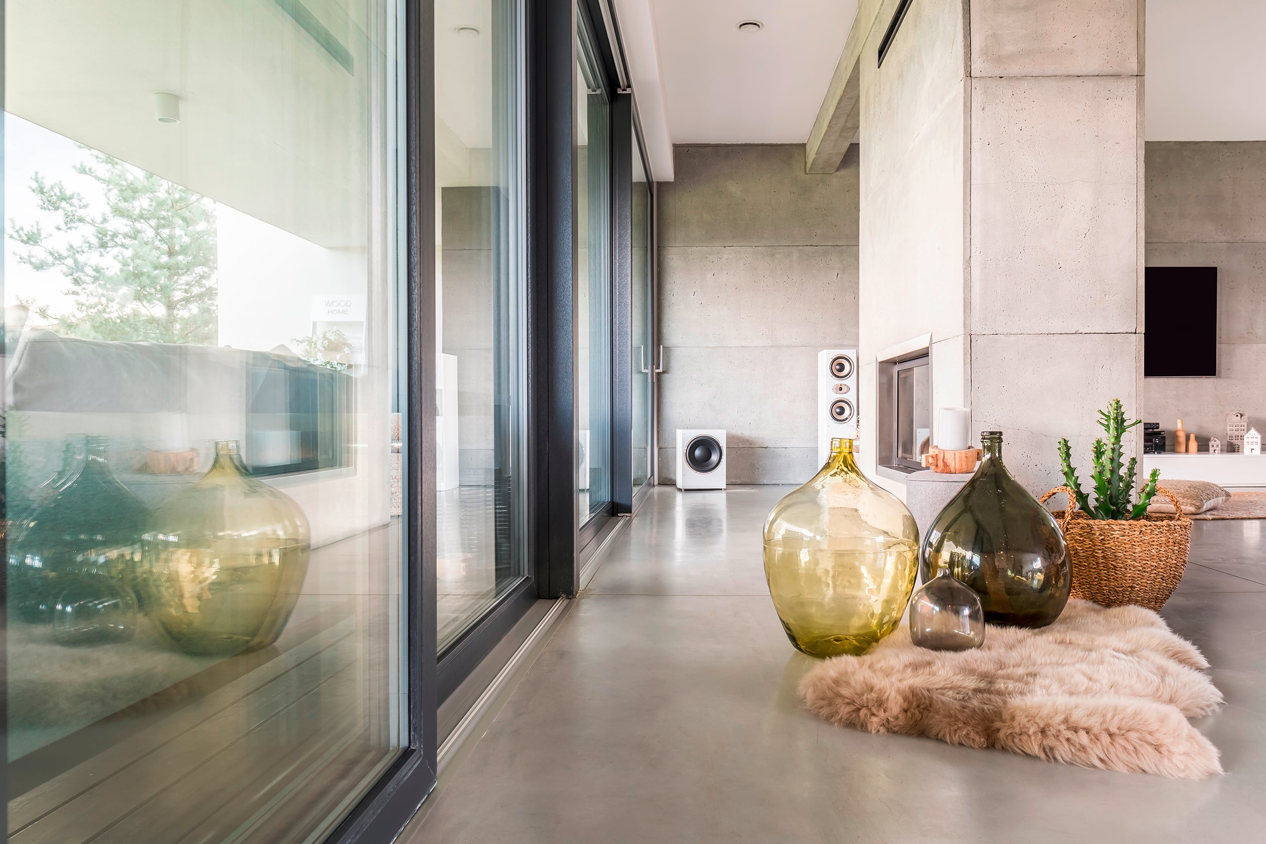 Moderner Wohnraum mit großen Ganzglas-Schiebelementen zur Terrasse, großen überformatigen Bodenfließen in Grau und einem freistehenden Kamin mit Sichtbeton verkleidet.