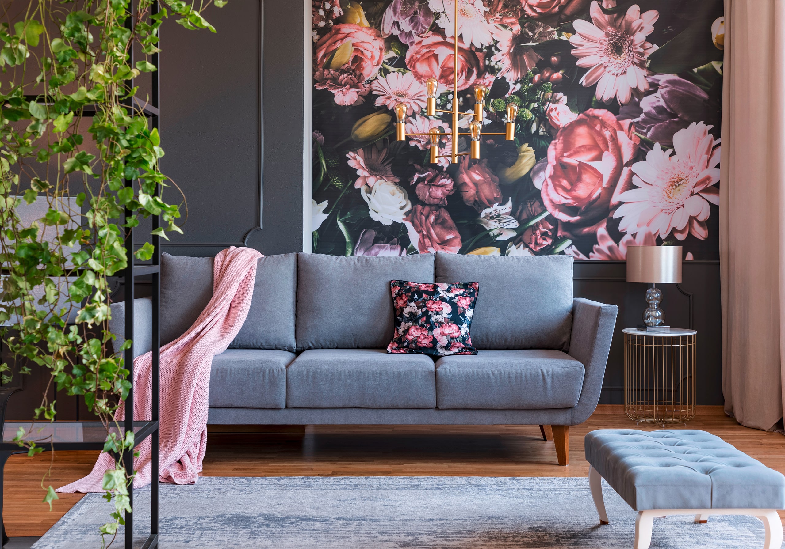 Klassisches Wohnzimmerinterieur mit extravaganter, farbenfroher Tapete mit Blüten, einem grauen Sofa aus Samt und Pflanzen.
