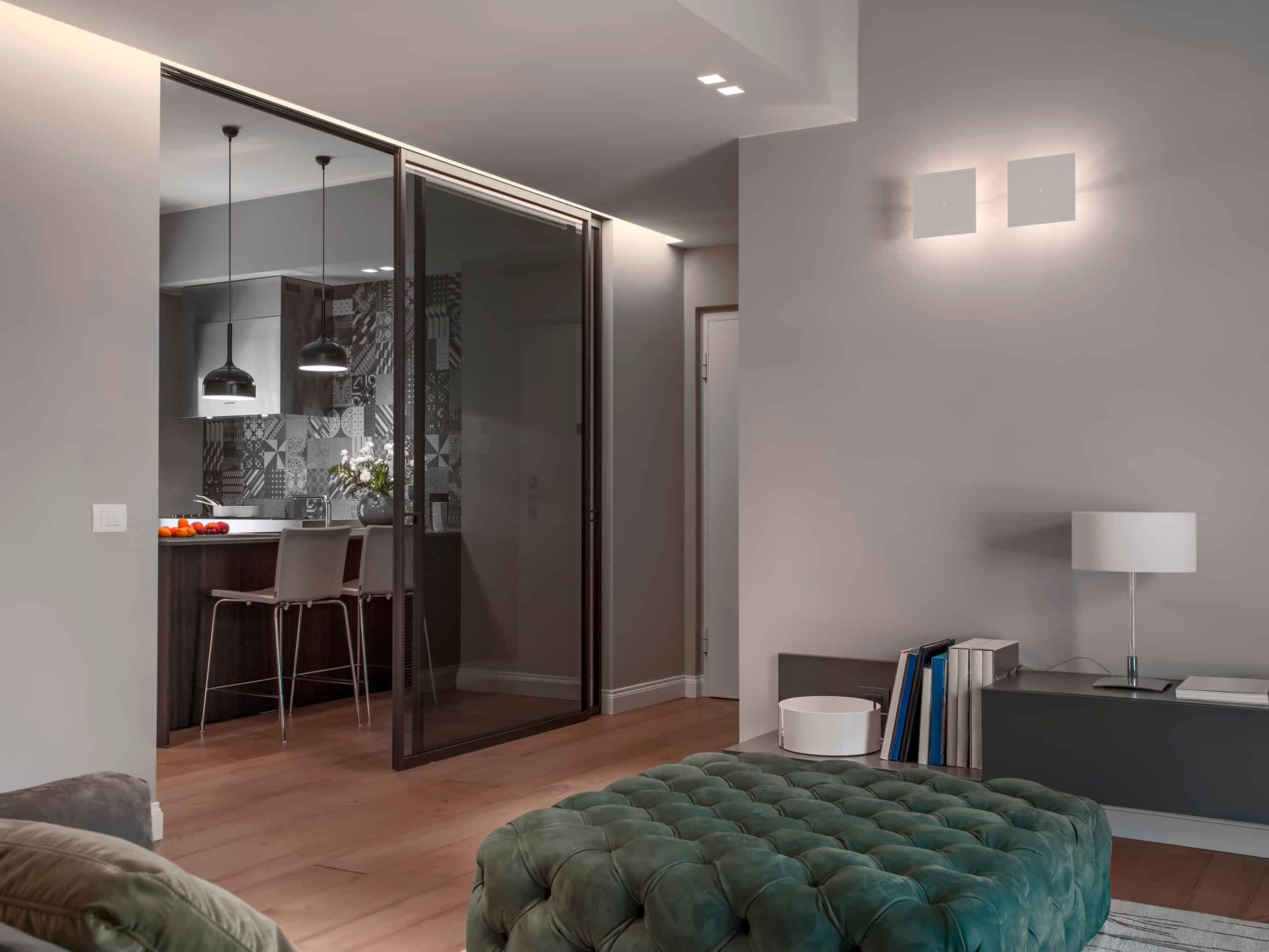 Innenansicht eines modernen Wohnzimmers mit Blick auf die Küche, die durch eine dezente Glasschiebetür mit satiniertem Schwarzglas smart abgetrennt werden kann.