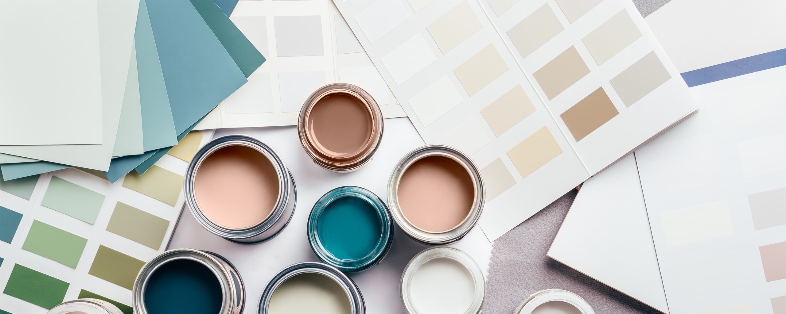 Kleine Metalldosen mit Farben und Lacken während der Hausrenovierung. Auswahl der Wandfarbe, „Mocha Mousse“ als Farbe des Jahres 2025, Farbkarten im Hintergrund.