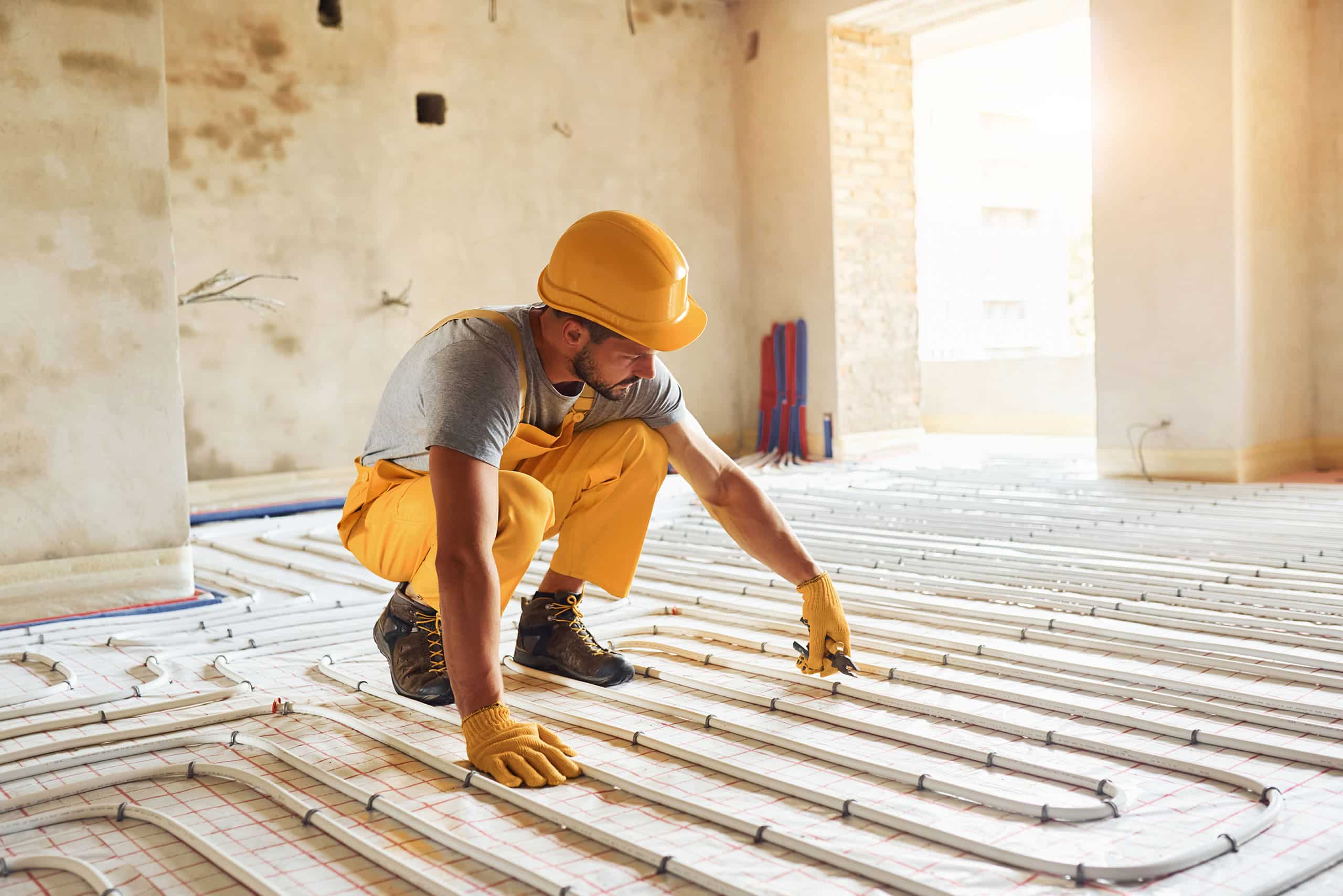 Arbeiter in gelber Arbeitskleidung installiert Fußbodenheizung in einem Altbau.