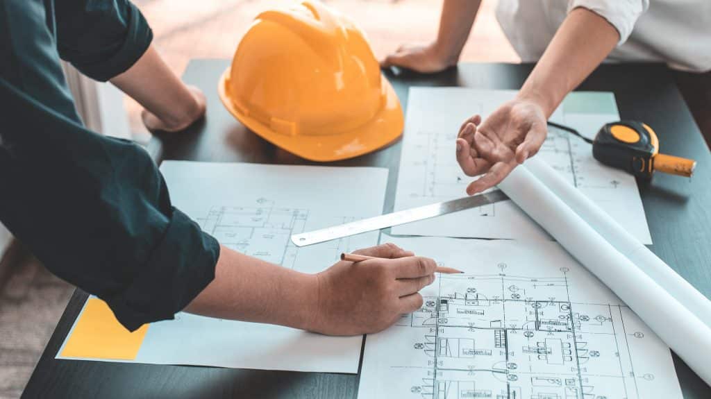 Treffen von Ingenieuren und Architekten zur Gebäudeplanung, Beratung und Brainstorming von Experten in der Architekturplanung unter Verwendung von Bauplänen, Maßbändern, Linealen und Laptops beim Entwerfen von Gebäuden.