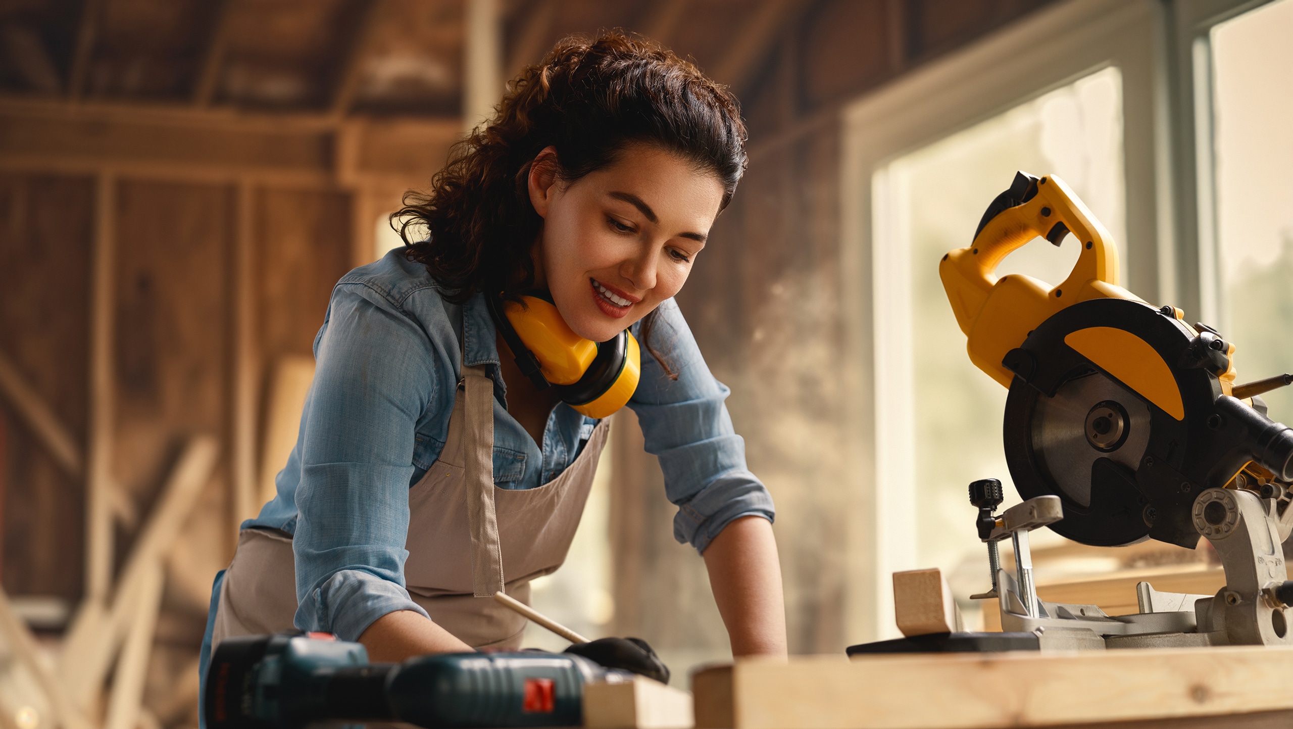 Junge Frau bzw. Tischlerin arbeitet gerade an einem Werkstück aus Holz, für welches sie eine Kappsäge benötigt.