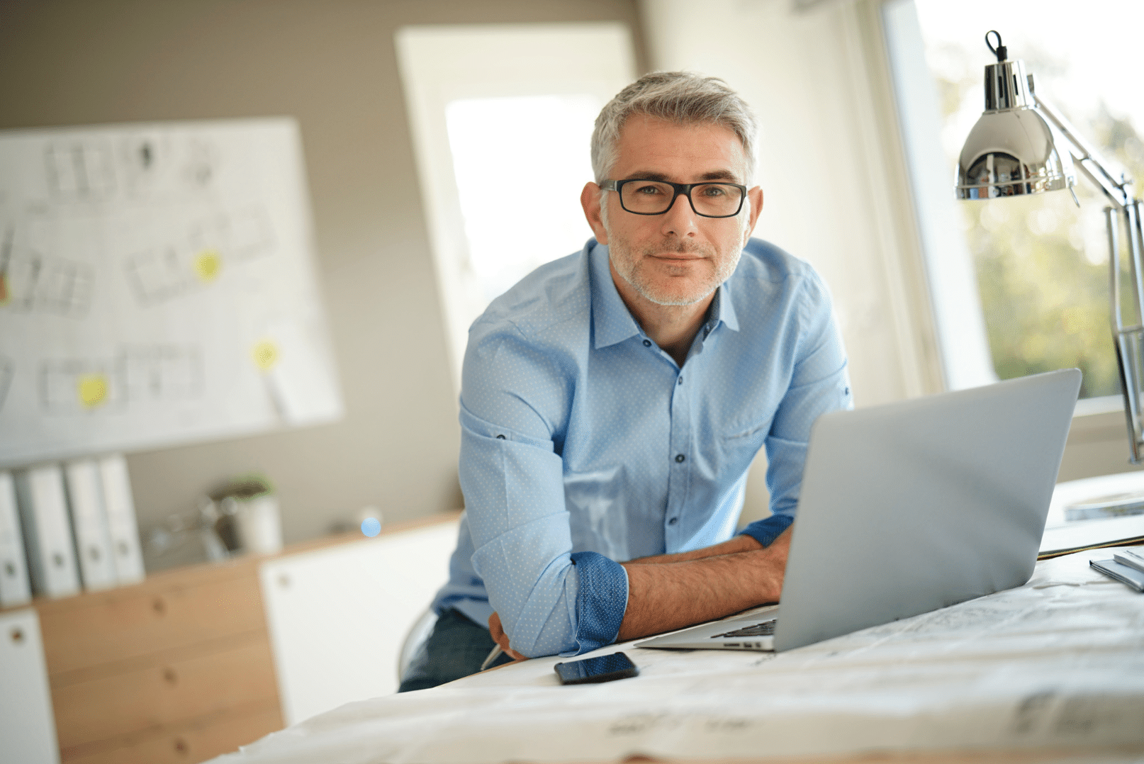 Architekt und Baumeister lehnt am Zeichentisch mit Laptop und kümmert sich um die Planung, Bauausführung und Neubau sowie Sanierung und Renovierung von Häusern und Gebäuden..