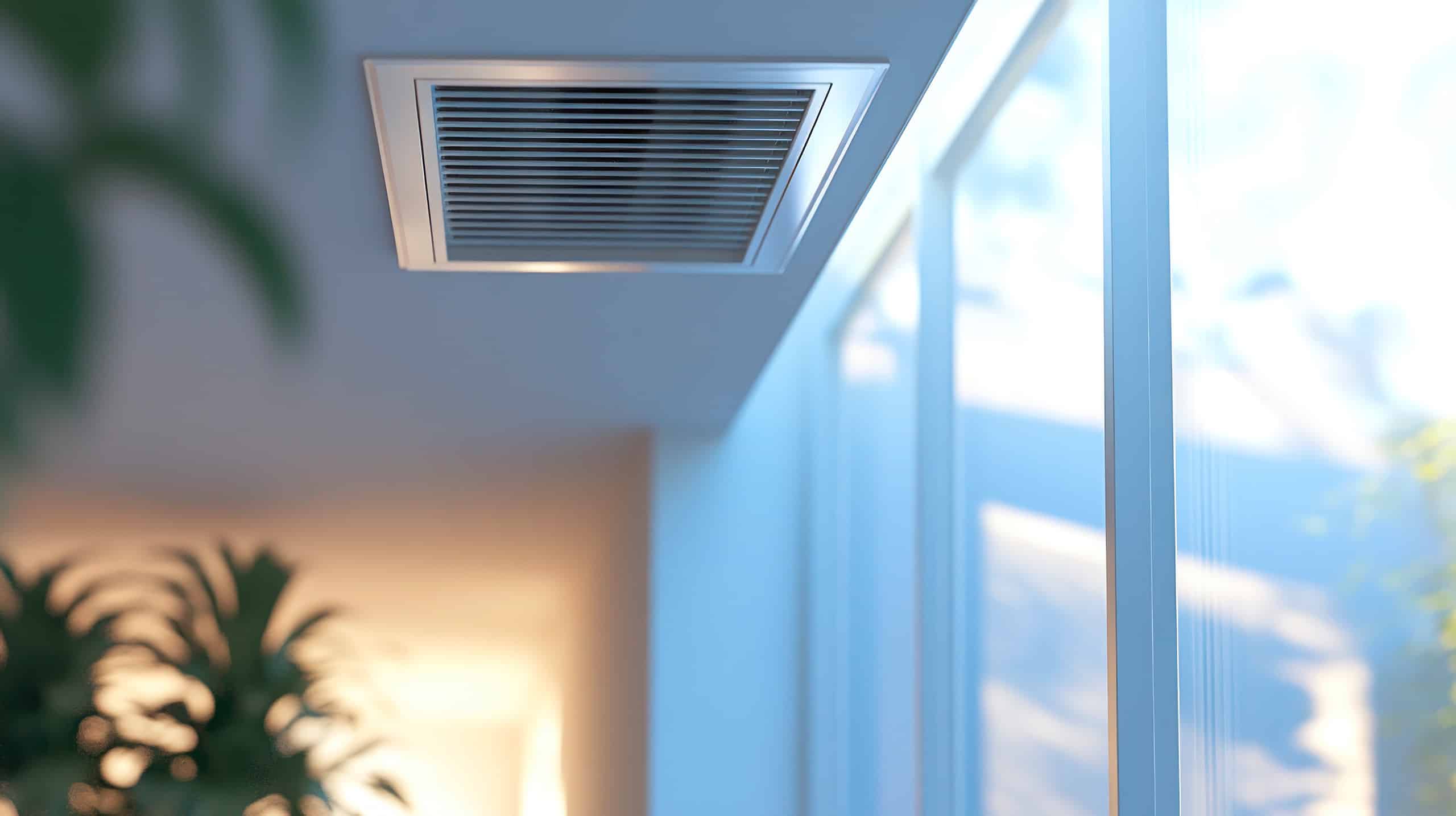 Detailansicht einer an der Decke installierten Wohnraumbelüftung nahe der großzügigen Fensterflächen eines modernen Wohnraumes.