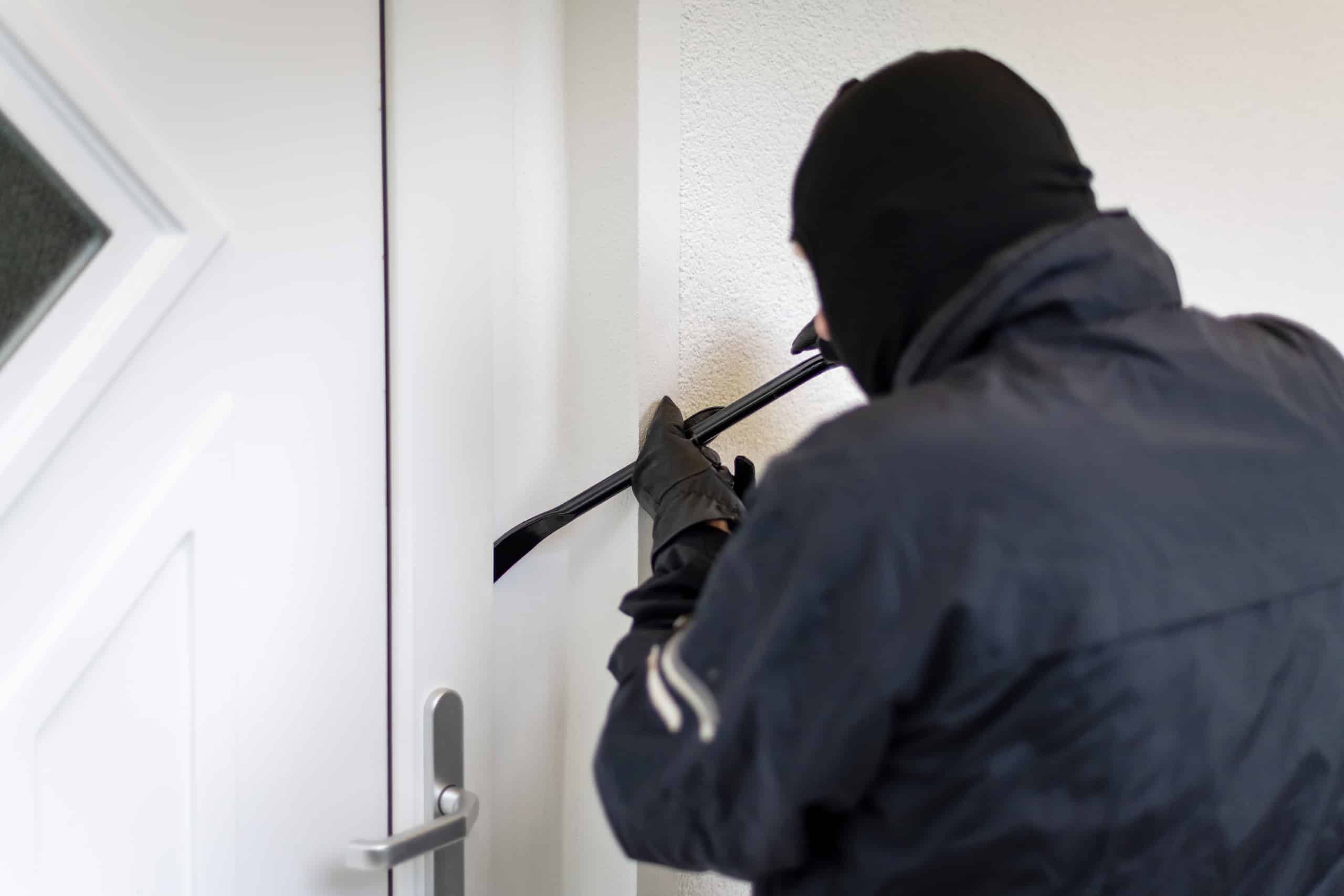 Ein Einbrecher, der versucht eine Hauseingangstür mit einem Brecheisen aufzubrechen.