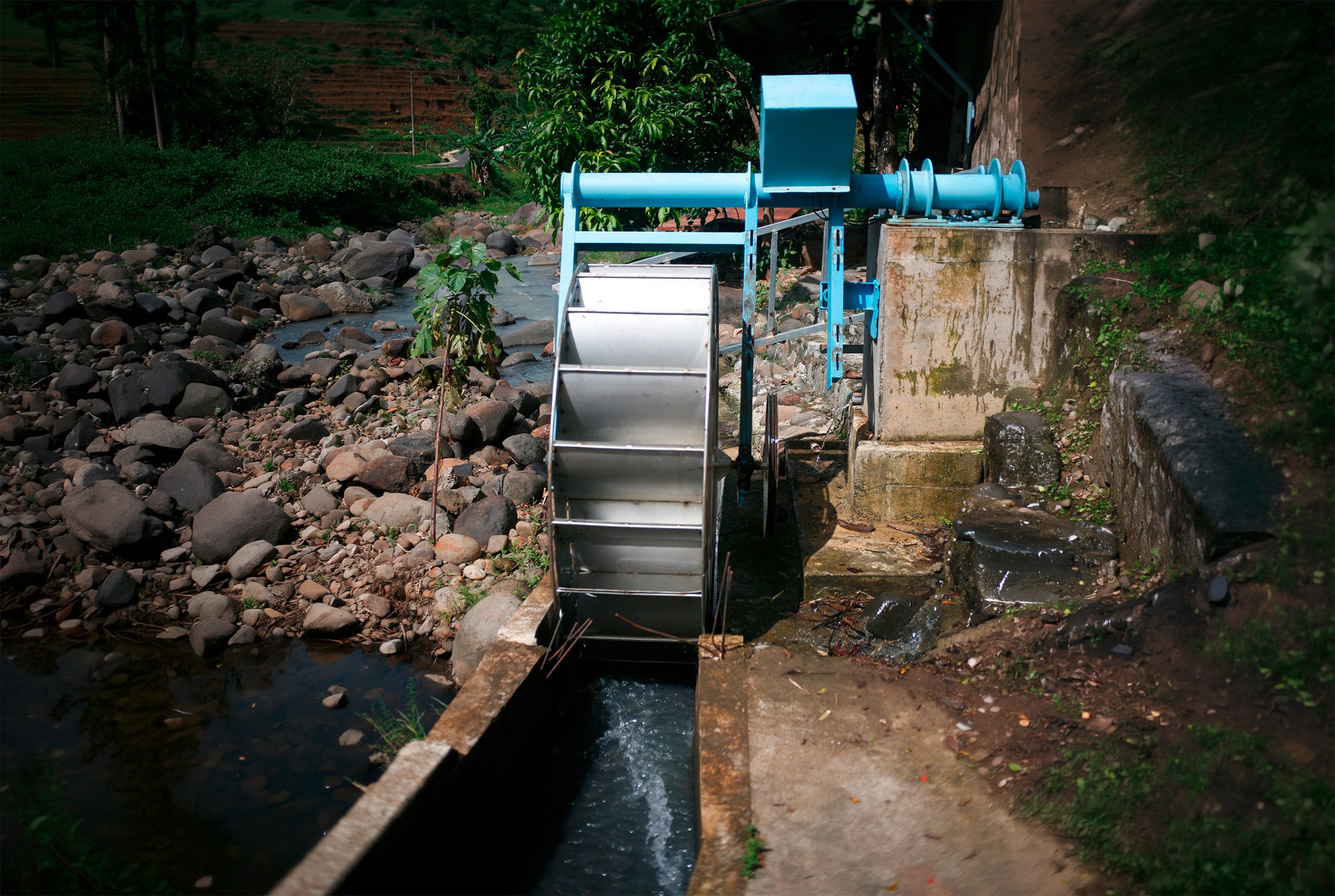 Kleinwasserkraftwerk mit einem Wasserrad aus Metall an einem kleinen Flusslauf zur Gewinnung von Strom für den privaten bzw. landwirtschaftlichen Verbrauch.