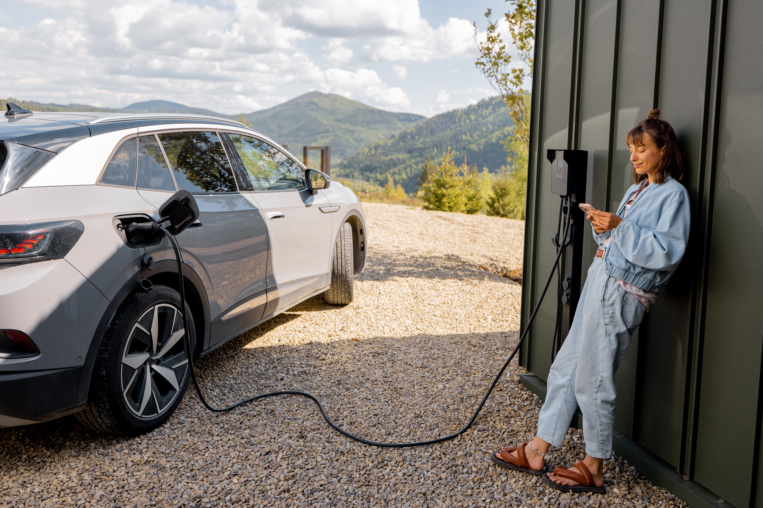 Frau schaltet Autoladestation ein, während sie ihr Elektrofahrzeug direkt mittels Wallbox an der Hausfassade auflädt und nutzt dieses innovative Konzept intelligenter Technologien für komfortables Leben mit Elektroautos.