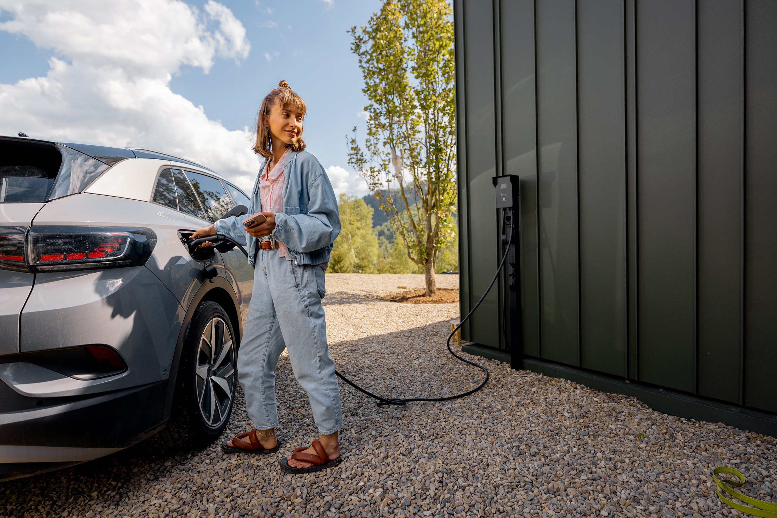 Frau schaltet Autoladestation ein, während sie ihr Elektrofahrzeug direkt mittels Wallbox an der Hausfassade auflädt und nutzt dieses innovative Konzept intelligenter Technologien für komfortables Leben mit Elektroautos.