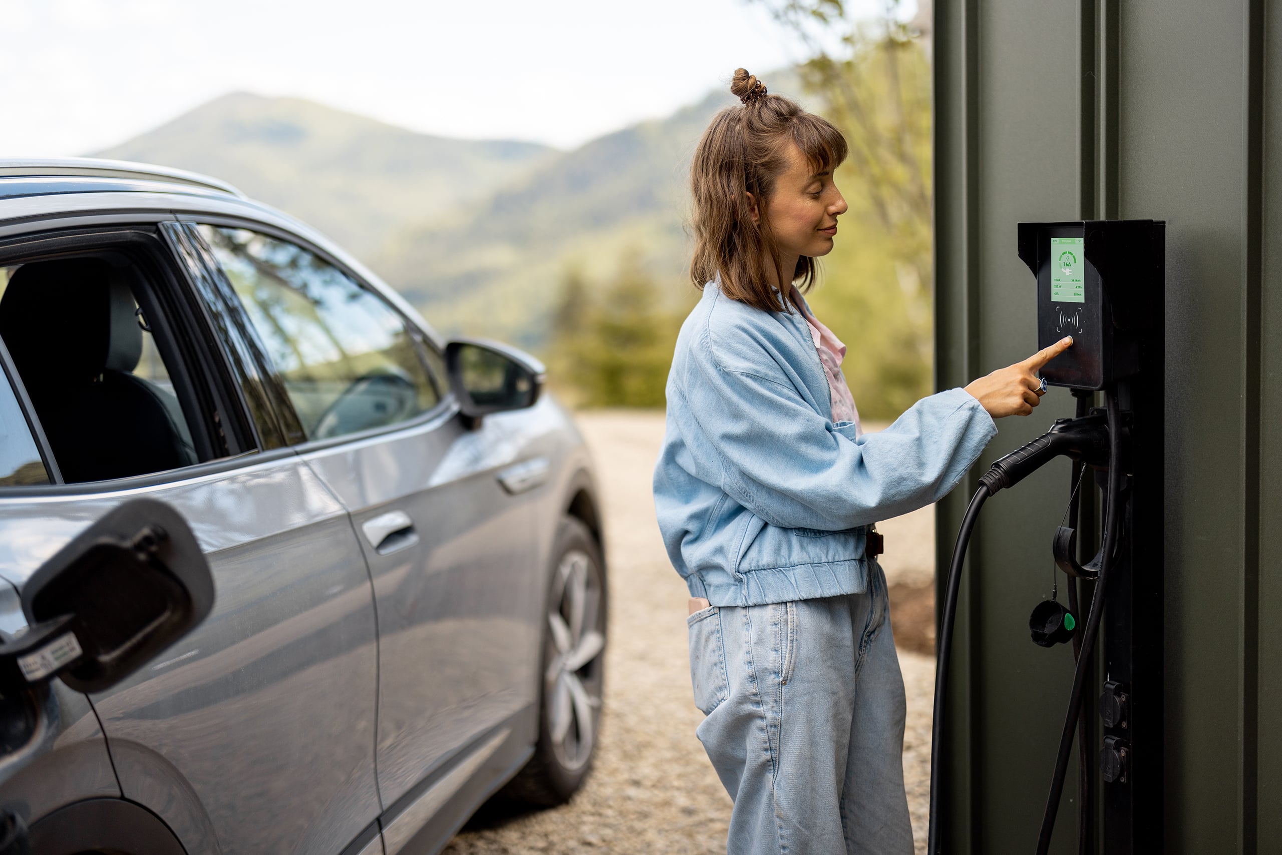 Frau schaltet Autoladestation ein, während sie ihr Elektrofahrzeug direkt mittels Wallbox an der Hausfassade auflädt und nutzt dieses innovative Konzept intelligenter Technologien für komfortables Leben mit Elektroautos.